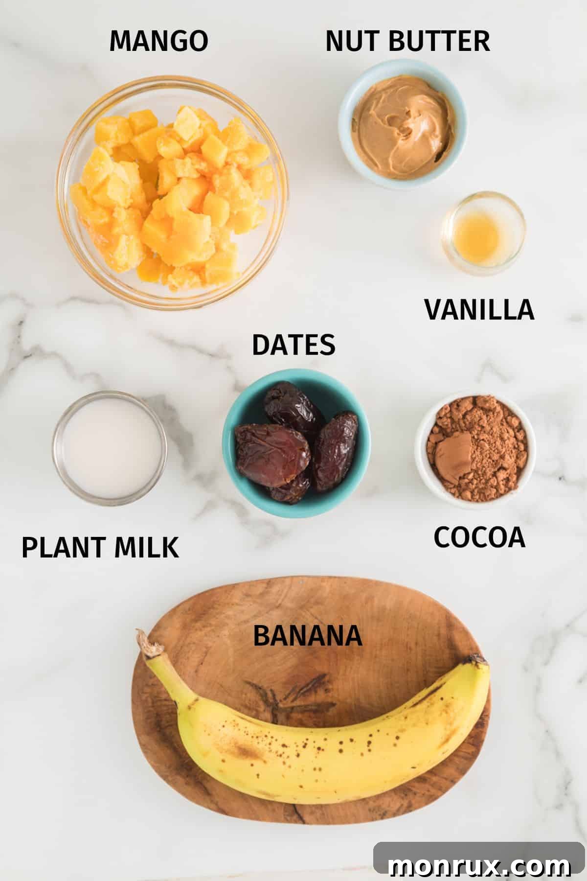 Arrangement of fresh and frozen ingredients including bananas, mango chunks, peanut butter, dates, cocoa powder, and almond milk for making dairy-free ice cream.