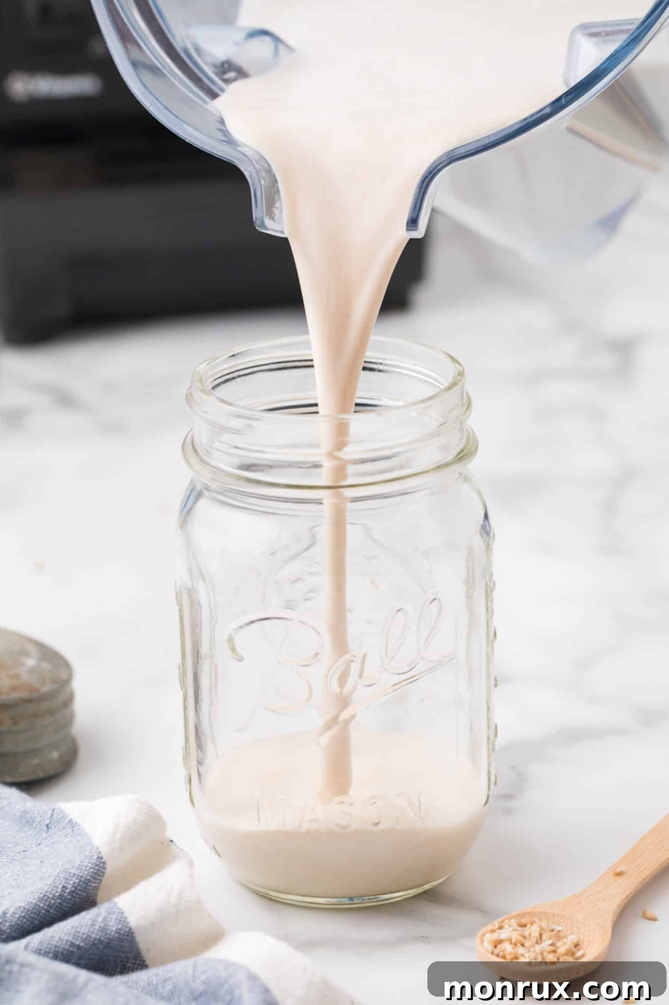 Freshly made homemade oat milk creamer being poured into a clear glass jar.