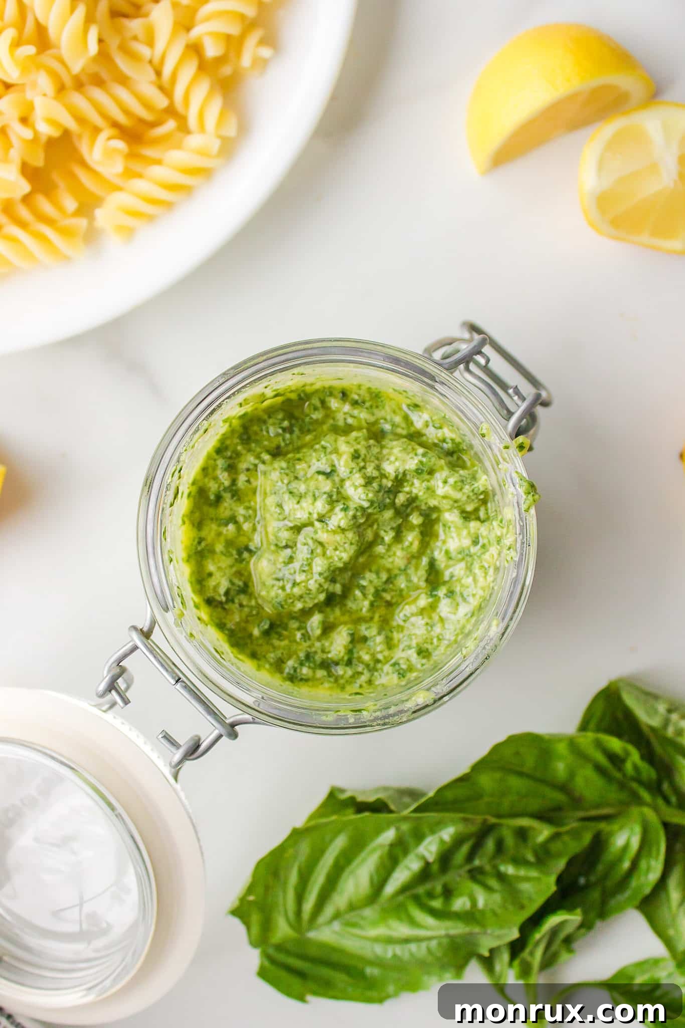 A close-up view inside a clear glass jar filled with luscious green dairy-free pesto sauce.