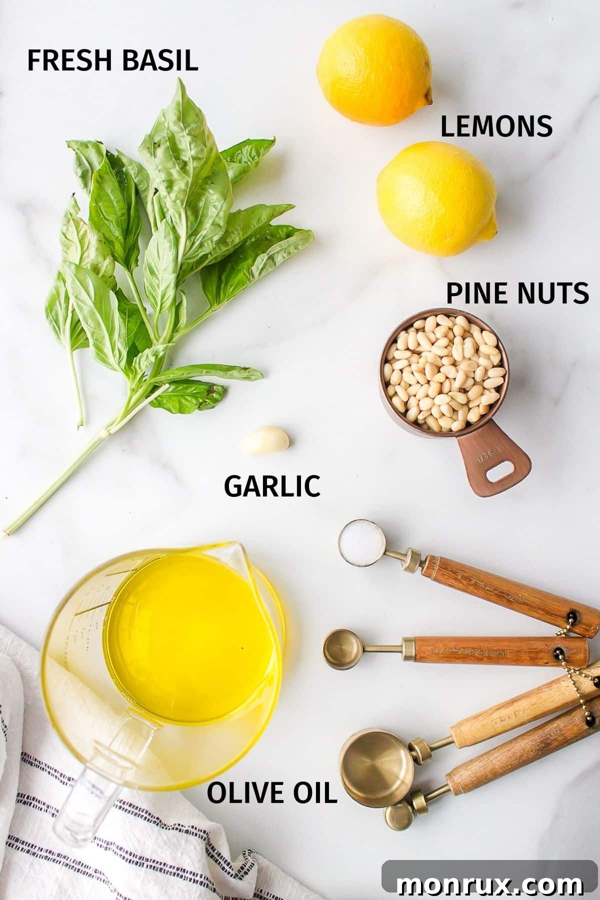 Fresh ingredients for dairy-free pesto, including basil, pine nuts, garlic, and lemons, arranged on a white surface.