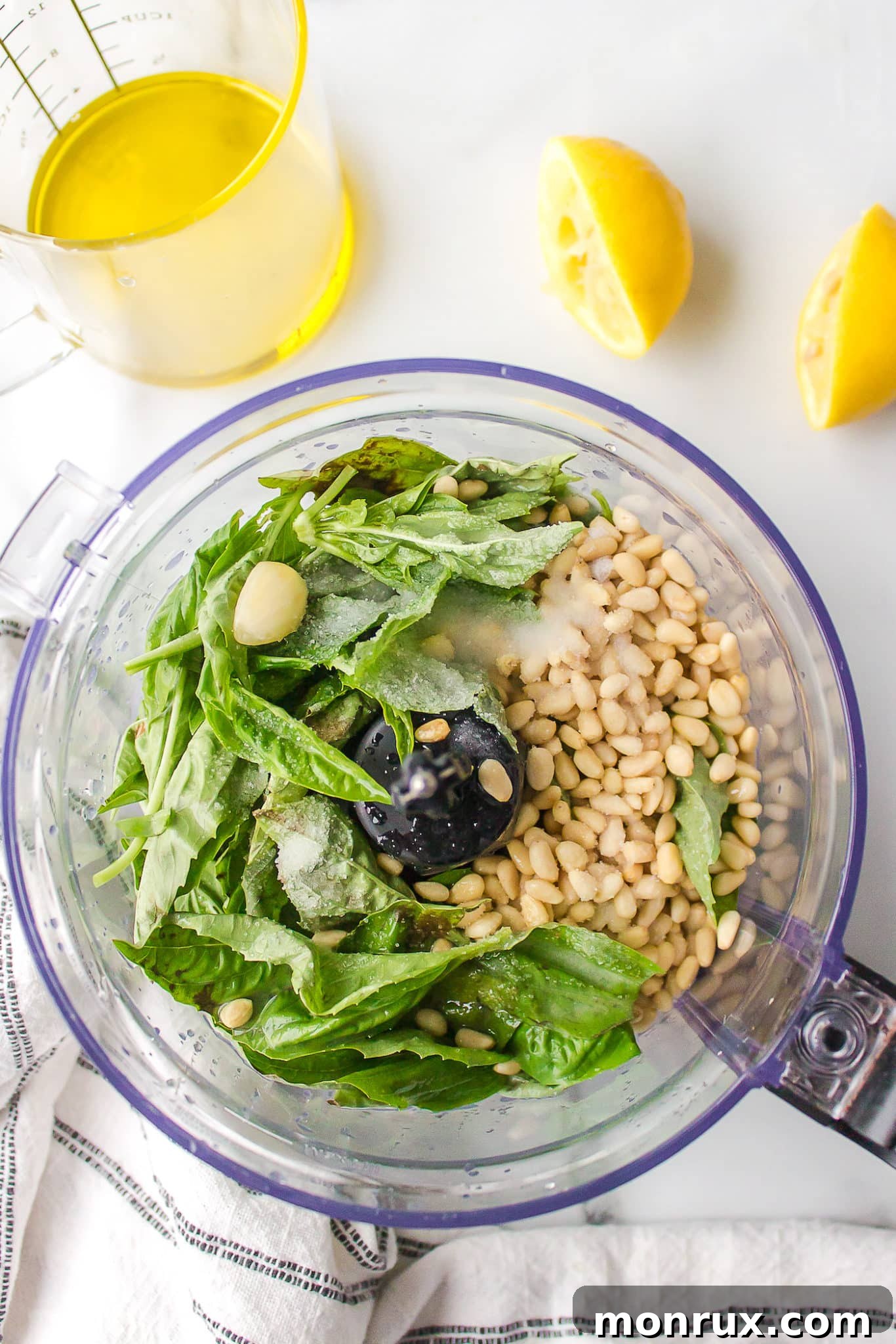 Fresh basil leaves and pine nuts placed in the bowl of a food processor, ready to be blended into pesto.