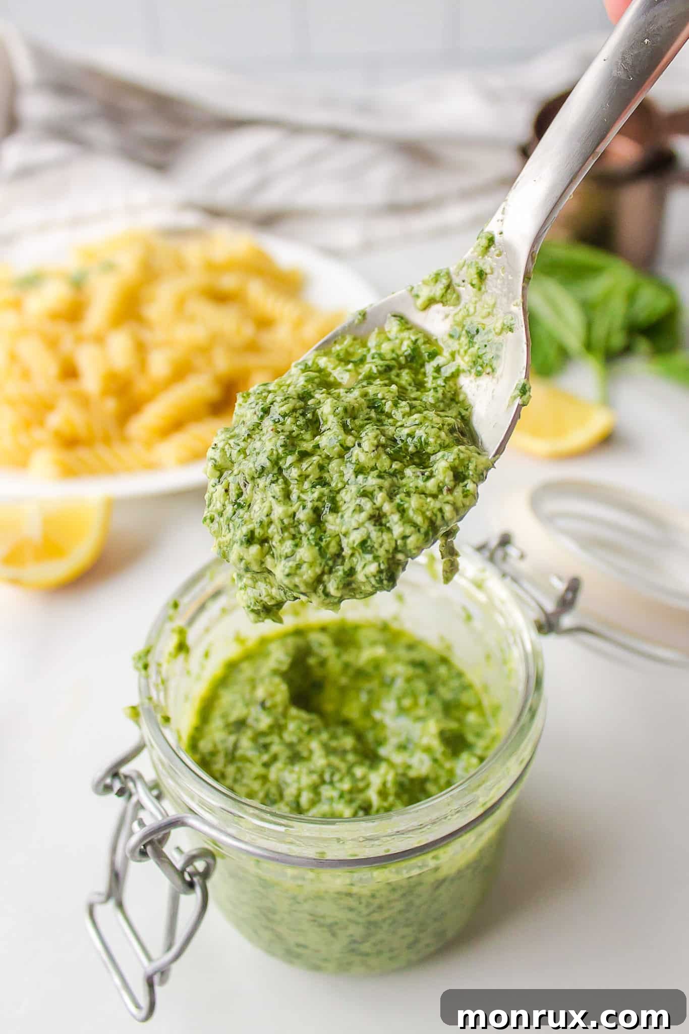 A spoon lifting a scoop of freshly made homemade pesto from a glass storage jar.