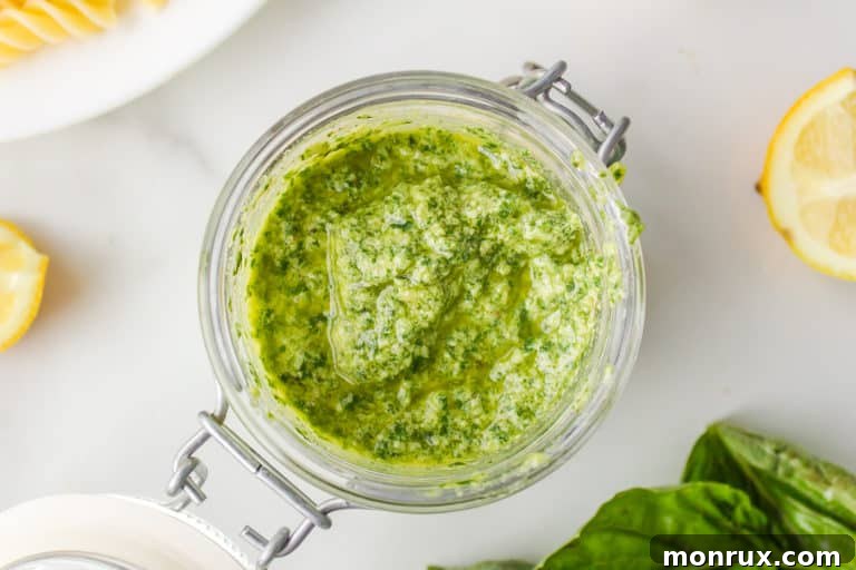 A close-up view of vibrant green pesto in a glass jar, with a spoon scooping some out.
