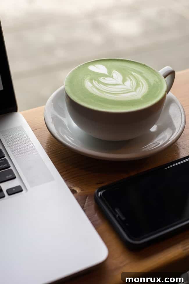 A vibrant green matcha latte sits beside a laptop computer, suggesting a perfect blend of work and wellness, enhancing focus and relaxation.