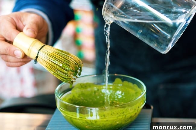 Preparing matcha tea by whisking hot water into the bright green powder in a traditional ceramic bowl, creating a smooth, frothy beverage.