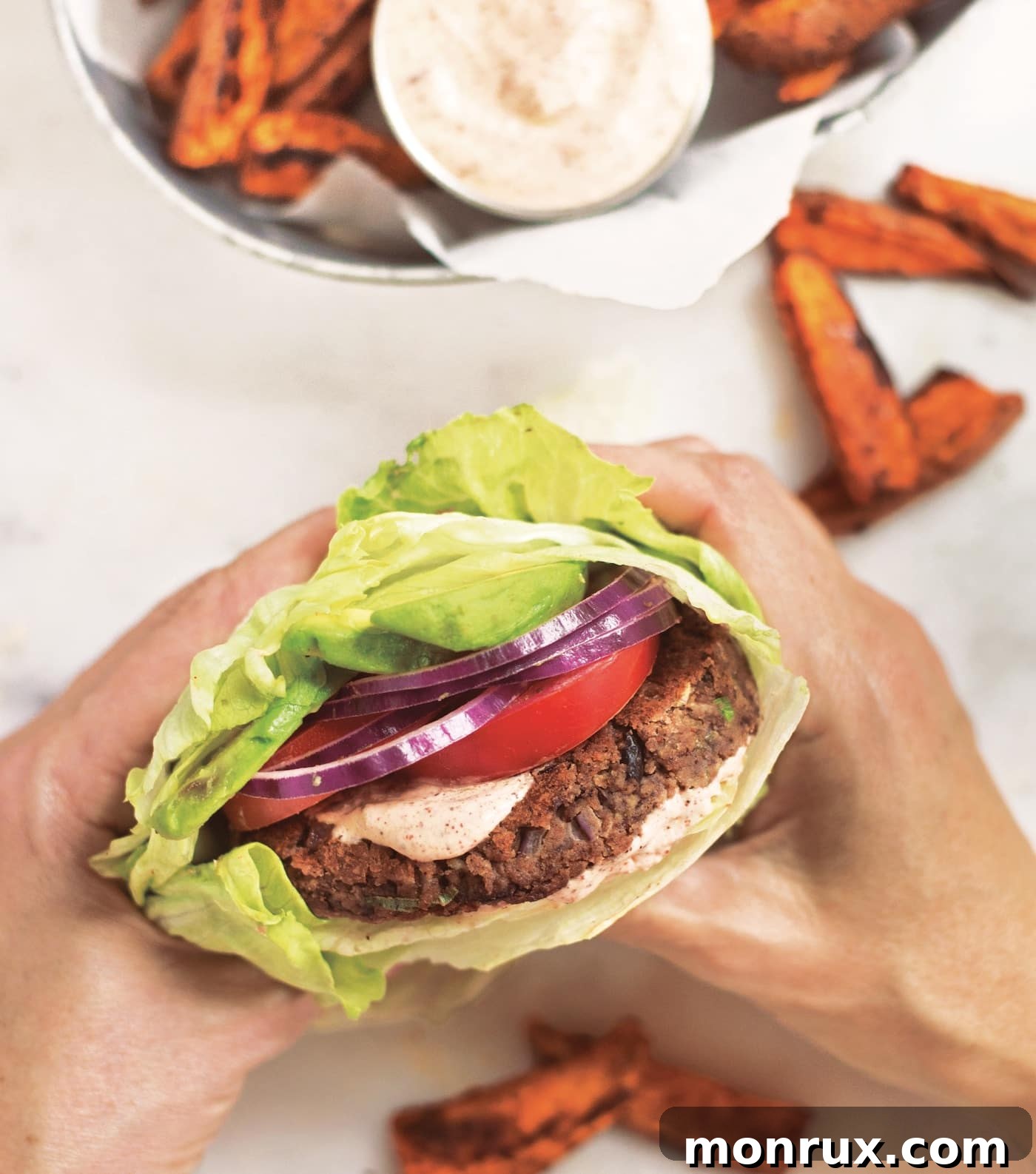 person holding a gluten-free black bean burger wrapped in lettuce, showcasing its delicious appearance.