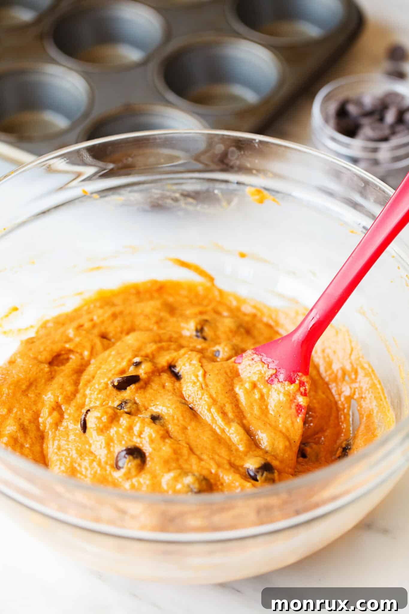 Rich orange gluten-free pumpkin muffin batter, speckled with chocolate chips, ready for the muffin tin.