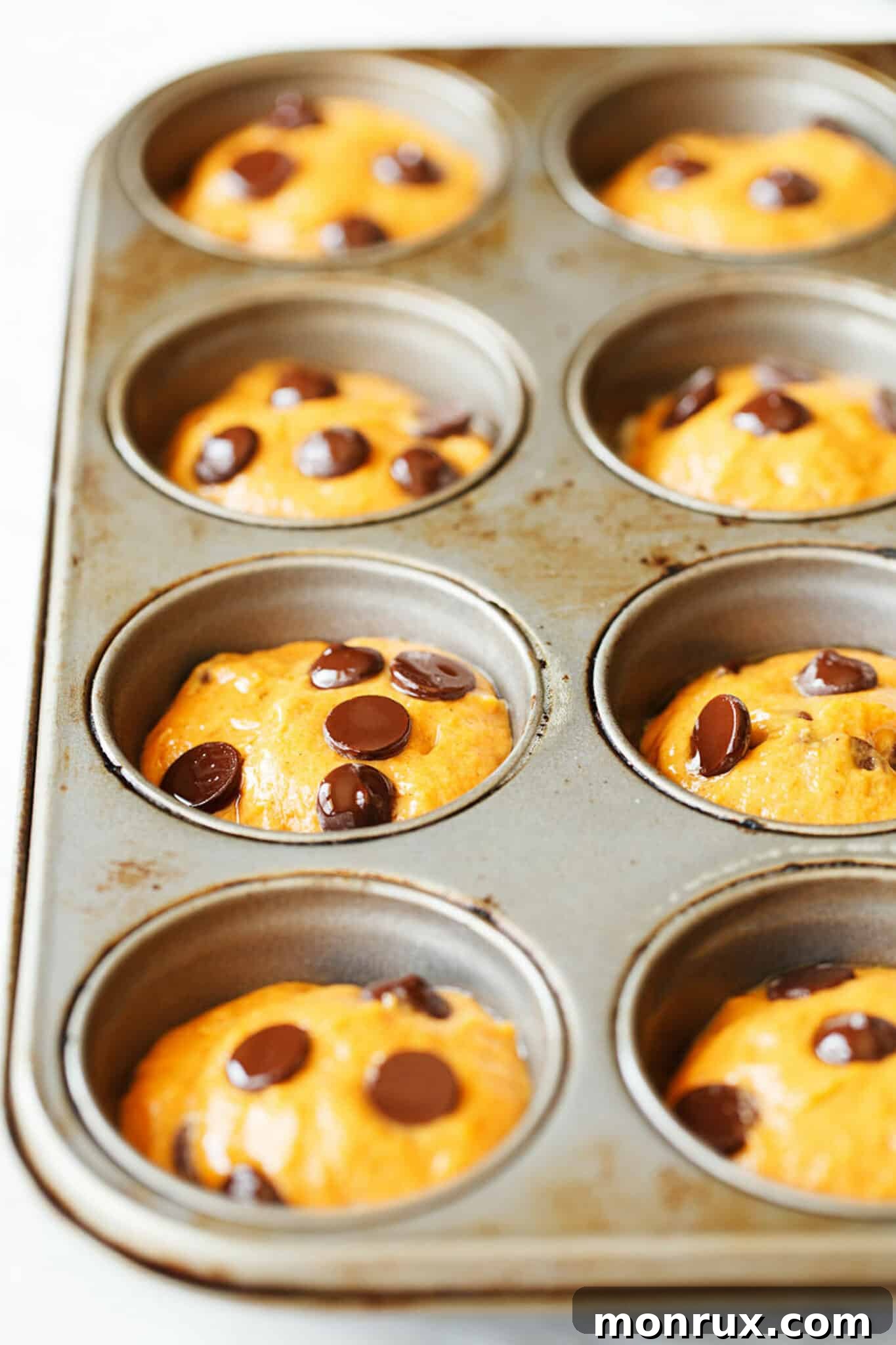 A muffin tray filled with unbaked gluten-free pumpkin muffin batter topped with chocolate chips, ready to go into the oven.