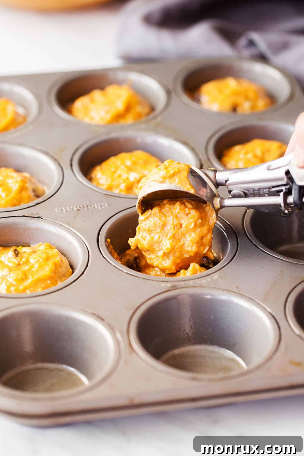 pouring sweet potato muffin batter in muffin tin.