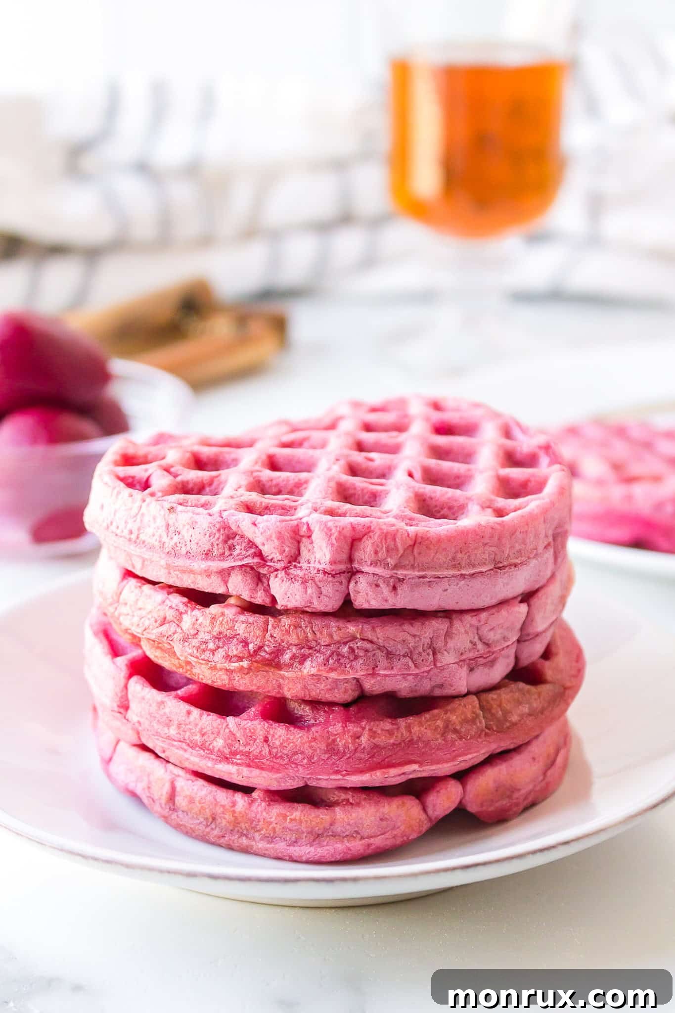 A stack of four fluffy pink waffles on a pristine white plate, garnished with a sprinkle of powdered sugar and fresh berries, ready to be enjoyed for a festive breakfast.