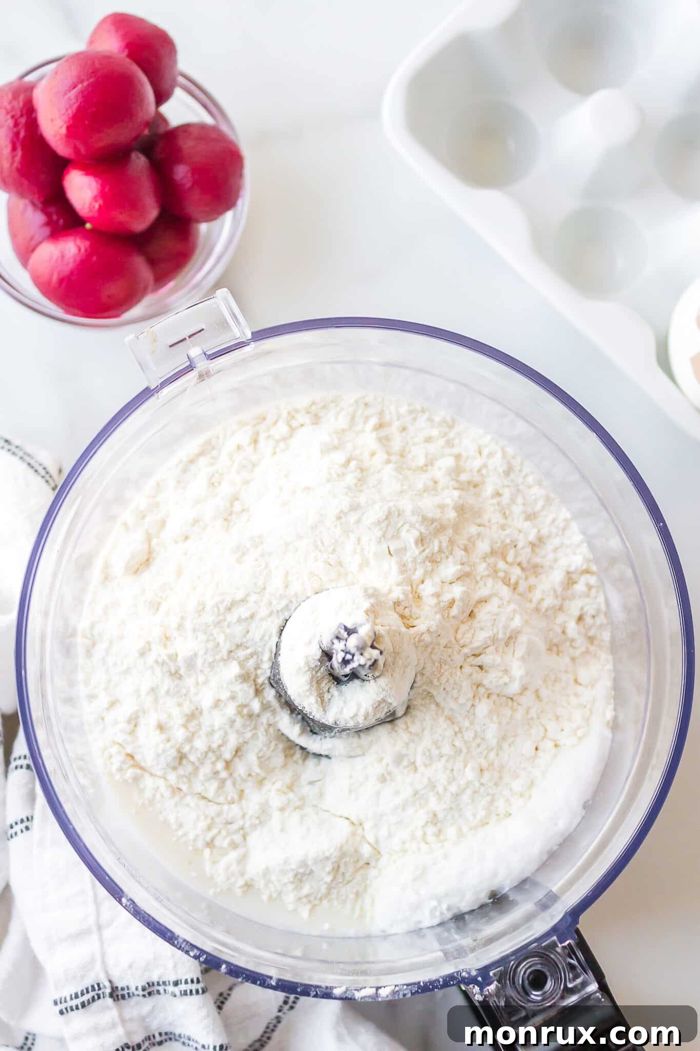 A bowl filled with dry ingredients for waffles, including flour and baking powder, ready for blending in a food processor.