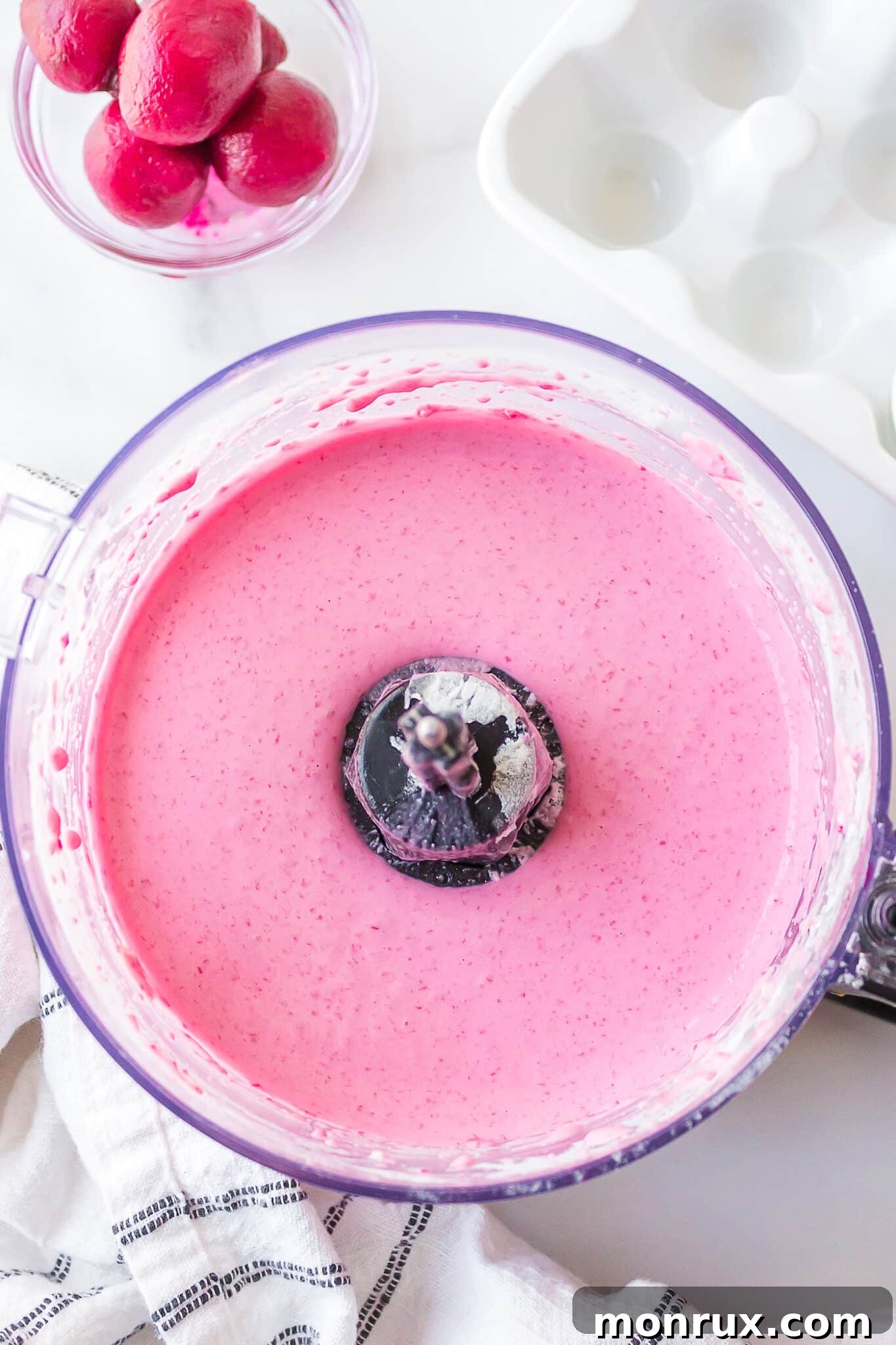 A smooth, pink batter swirling in a food processor, indicating that beets have been thoroughly blended with the flour and other ingredients.