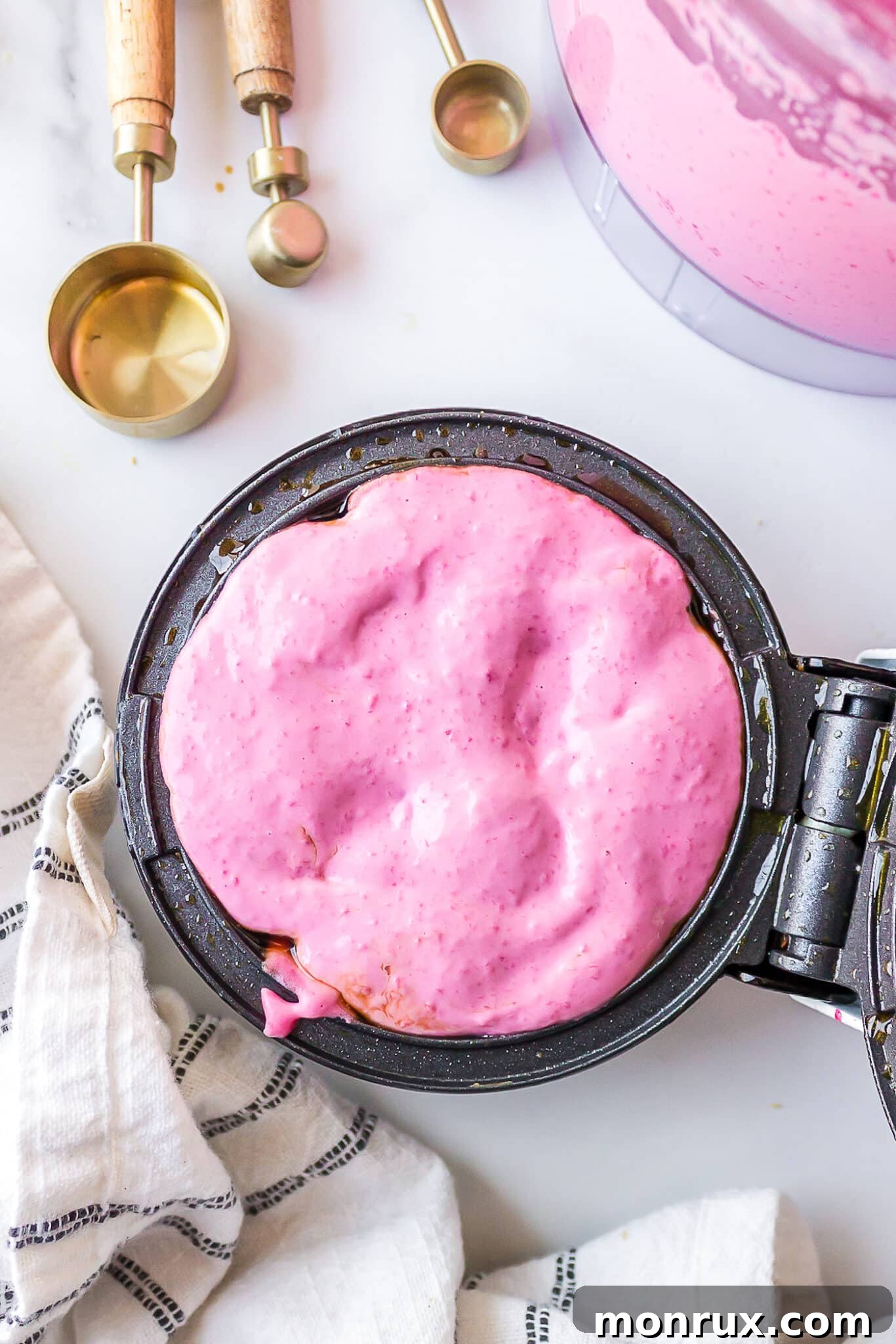 A close-up view of a hot waffle iron, with a vibrant pink batter being carefully poured onto its heated surface, ready for cooking.