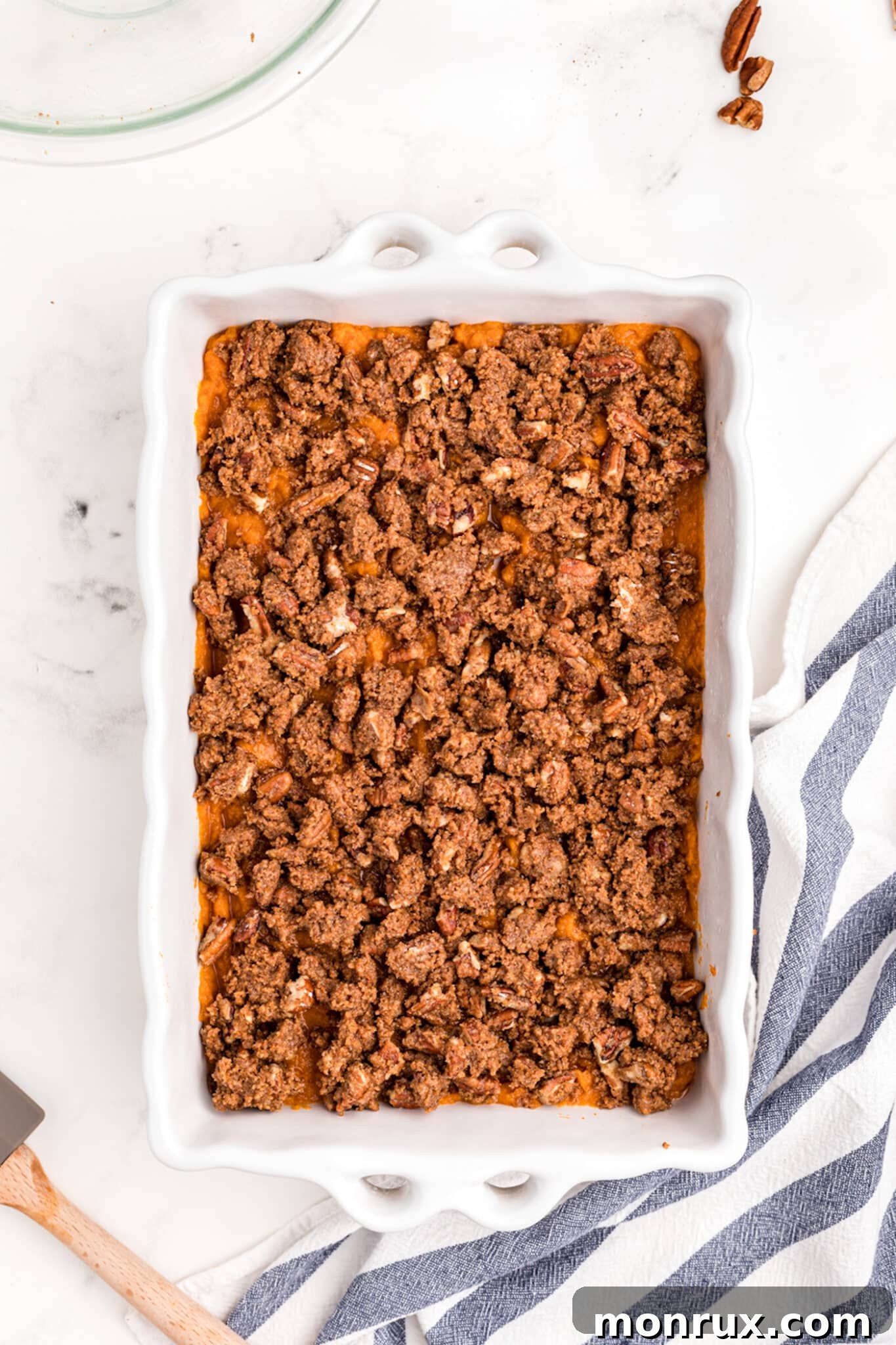 The sweet potato casserole in a baking dish, generously covered with a crunchy pecan crumble topping, prior to baking.