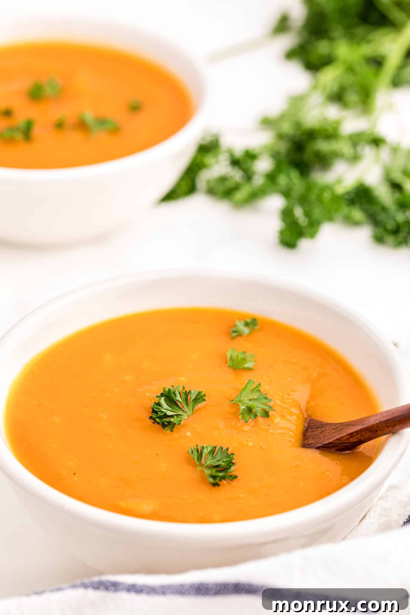Two white bowls filled with golden butternut squash soup, garnished with fresh herbs.