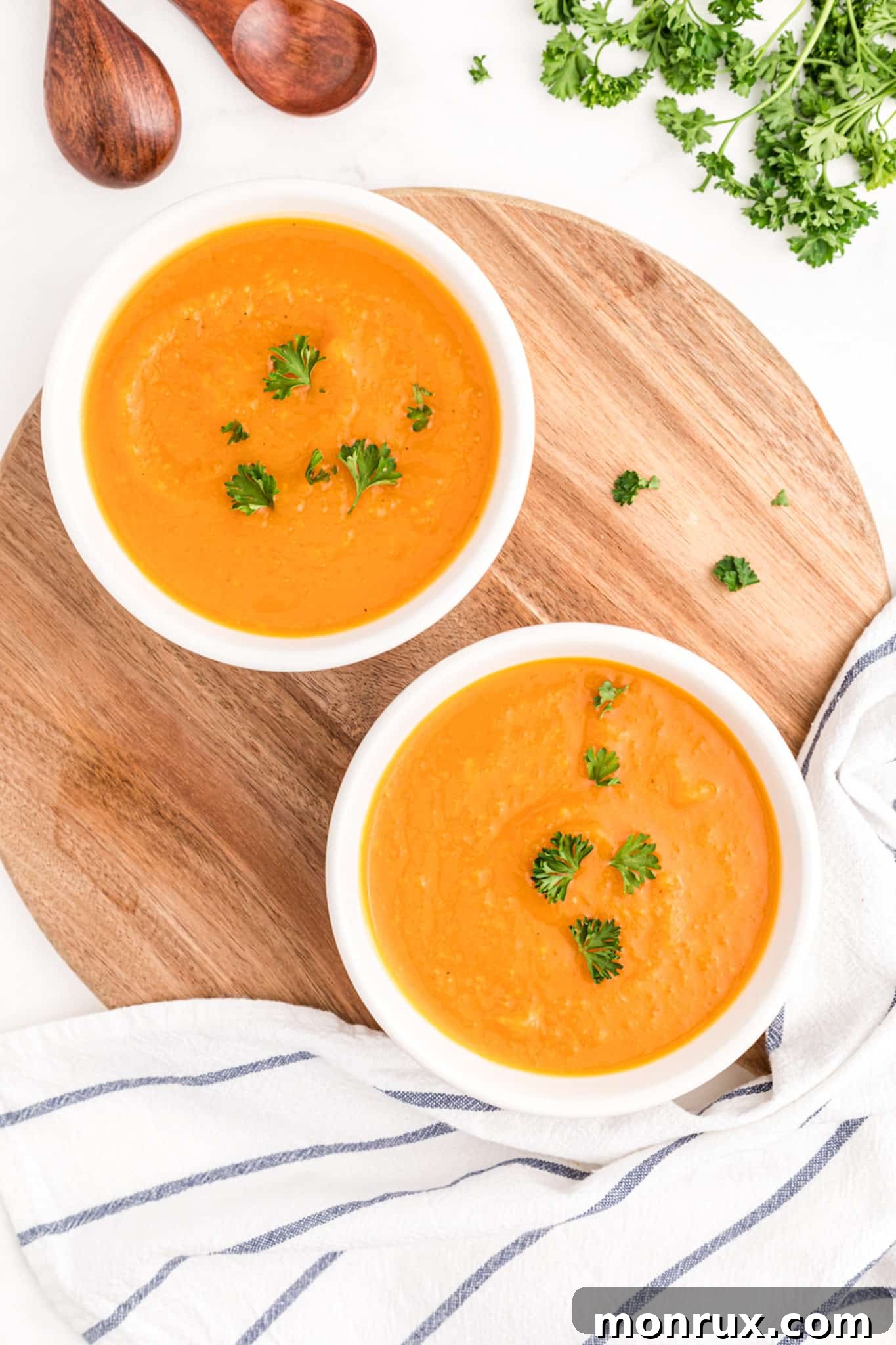 Close-up of butternut squash soup in a white bowl, garnished with a sprig of fresh parsley.