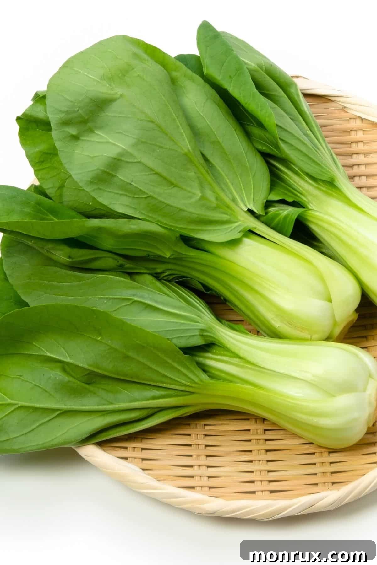 Fresh baby bok choy arranged neatly on a bamboo mat, highlighting its white stalks and green leaves.