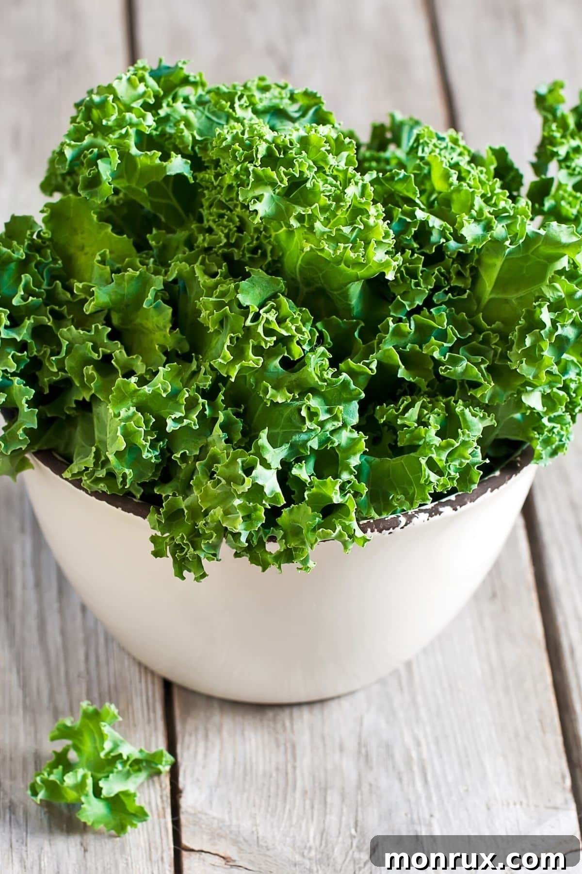 Fresh, curly green kale leaves in a white ceramic bowl on a light table, ready for preparation.