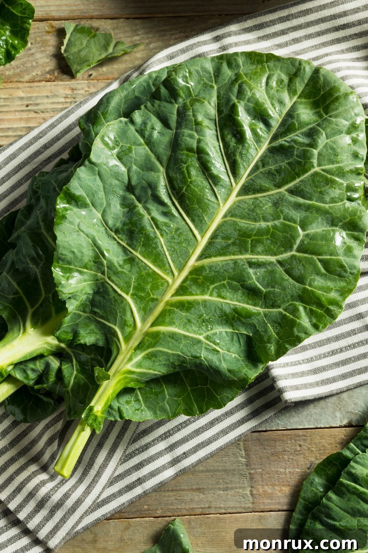 Large, broad collard green leaves spread on a wooden table with a kitchen towel, ready for preparation.