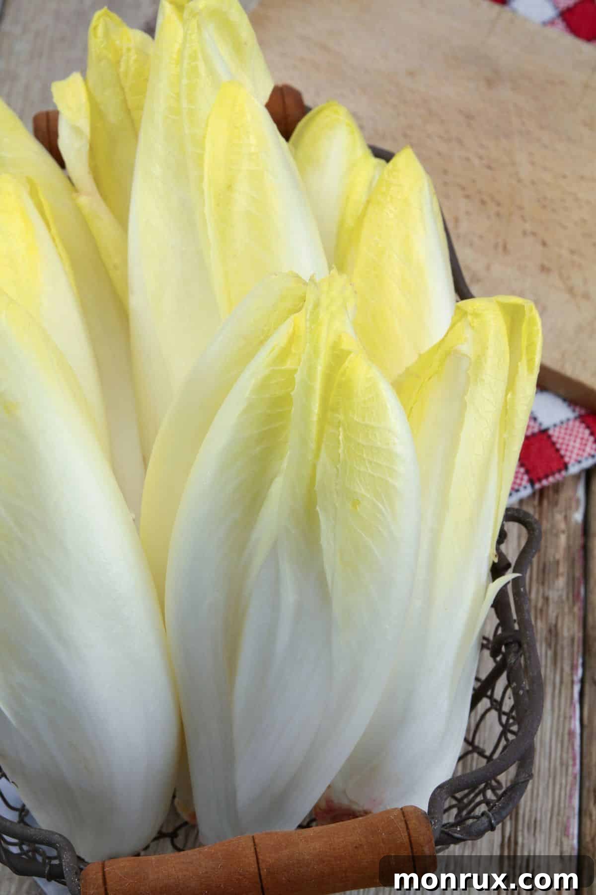 A head of fresh endive, showcasing its light green leaves and slightly bitter taste, on a wooden table.