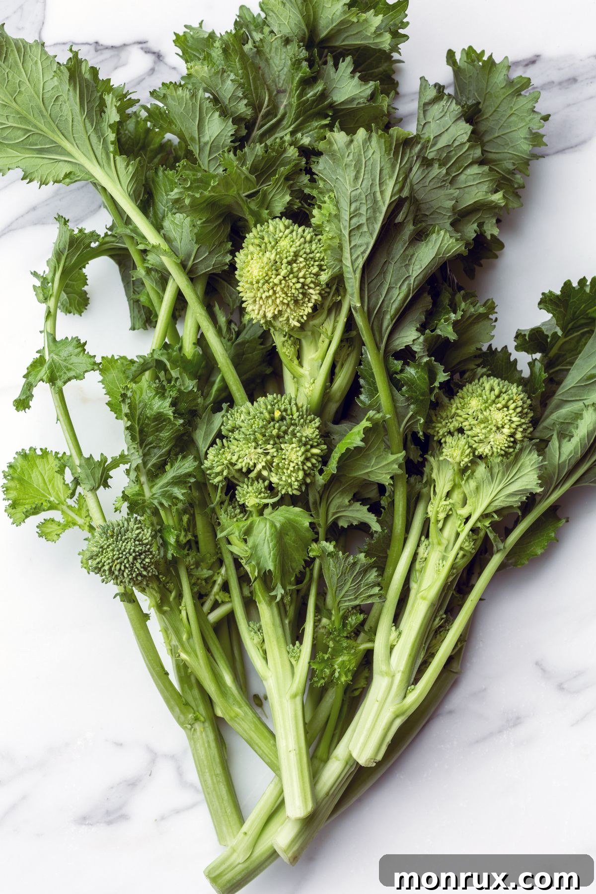 A bunch of fresh broccoli rabe on a wooden table, featuring small green buds and leafy stalks.