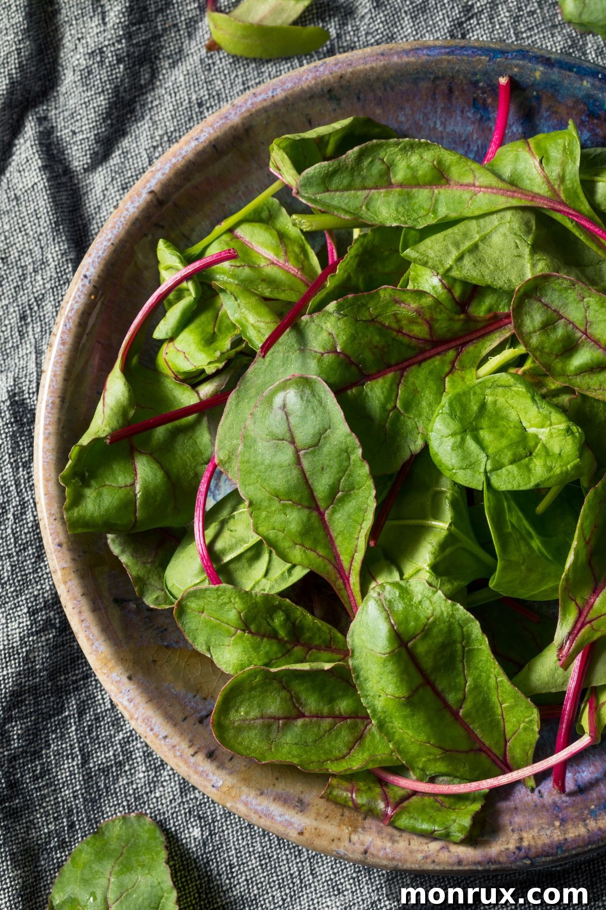 A bunch of vibrant beet greens with red stems on a wooden table, emphasizing their freshness.
