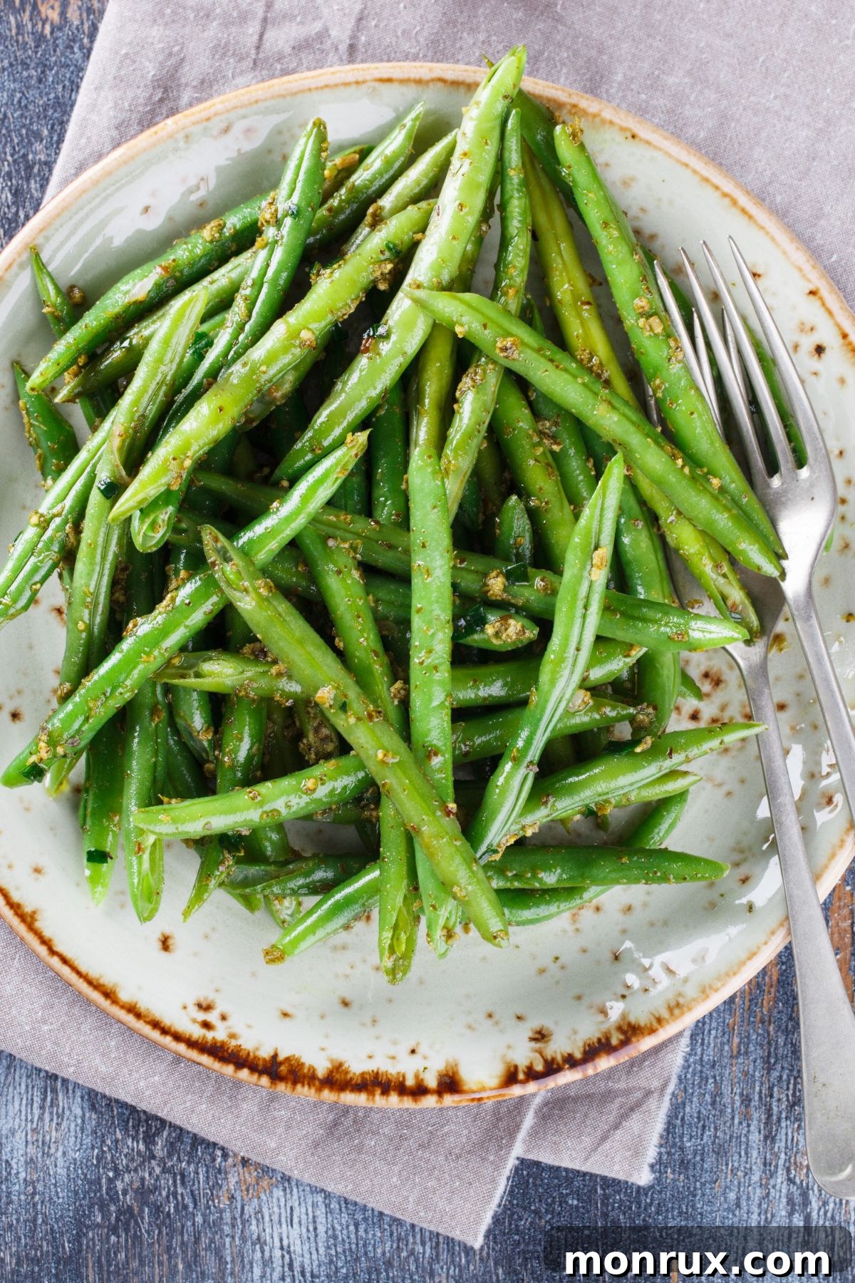 A serving bowl filled with vibrant green beans, lightly steamed and ready to eat, on a textured surface.