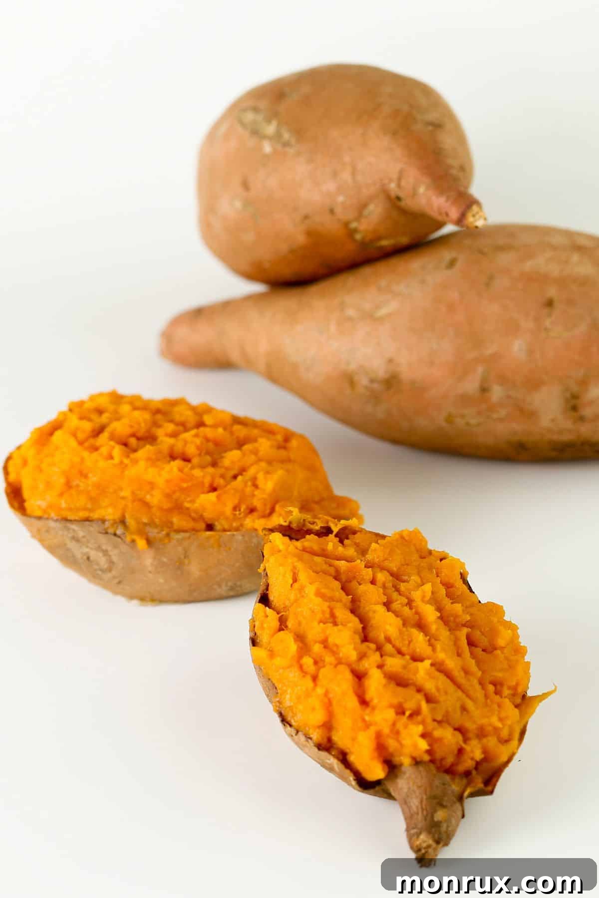 Two baked sweet potatoes, perfectly halved to reveal their bright orange, tender flesh, resting on a rustic wooden surface, ready to be mashed for baking.