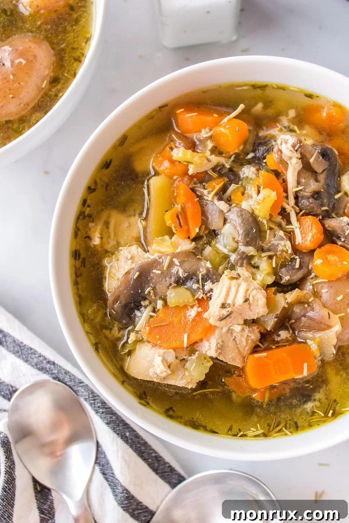 Hearty chicken soup with potatoes and vegetables in a rustic bowl, garnished with fresh herbs.