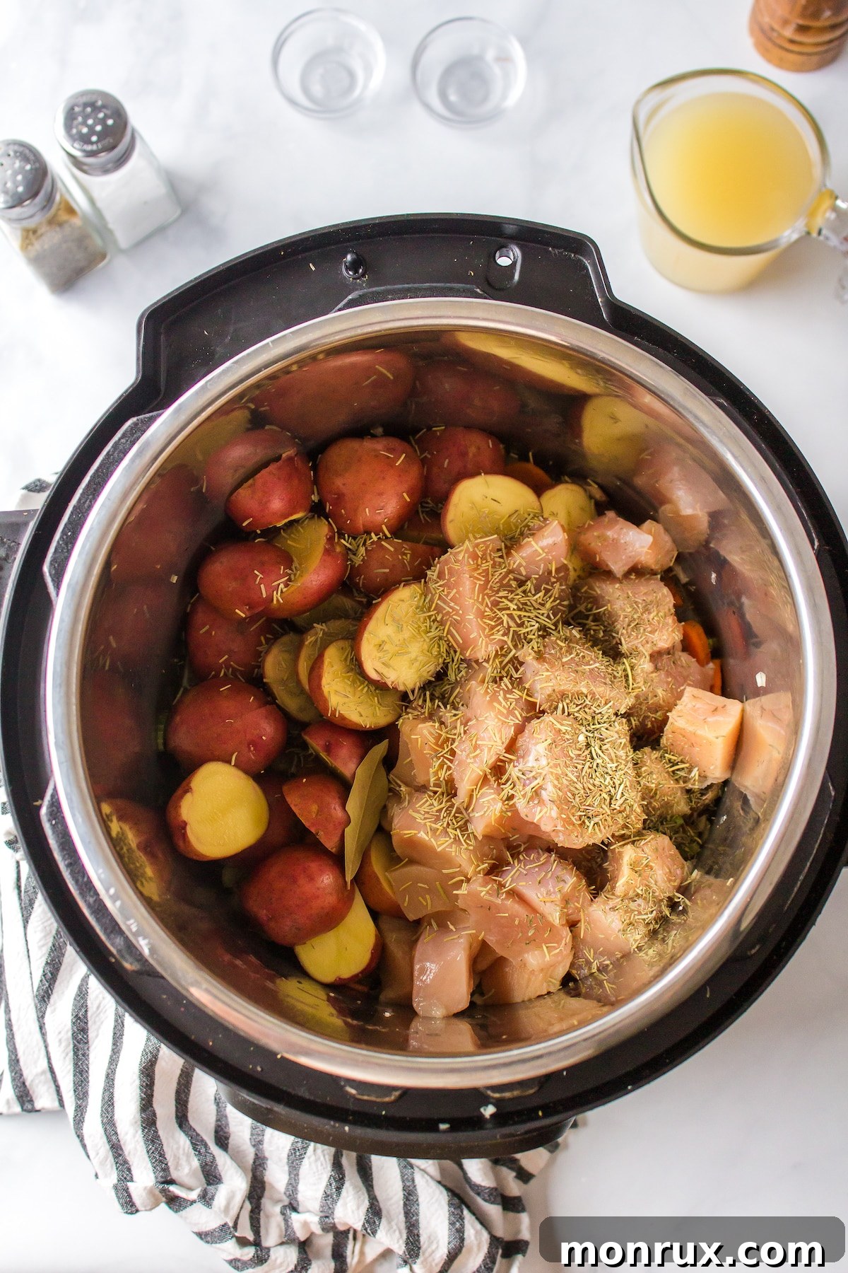 Chicken pieces and chopped potatoes being added to the sautéed vegetables in a pot.