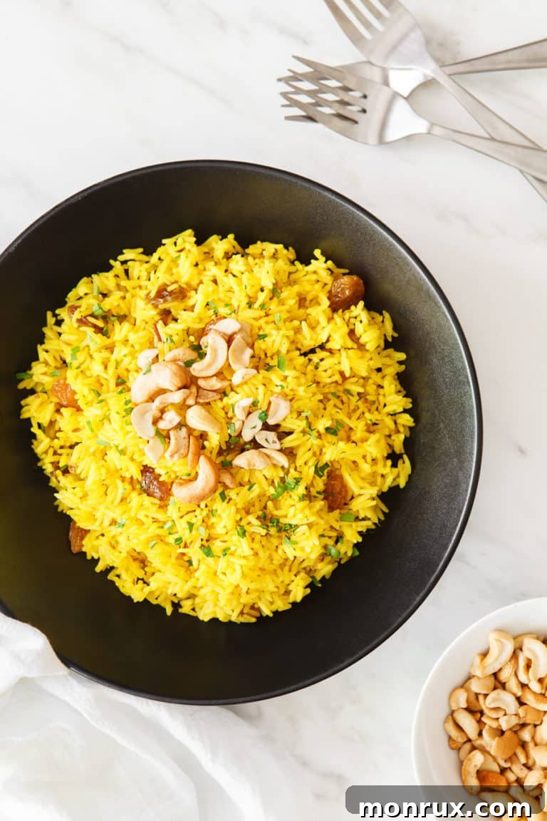 A serving of Indian Yellow Rice garnished with golden raisins and crunchy cashews, presented in a rustic bowl.