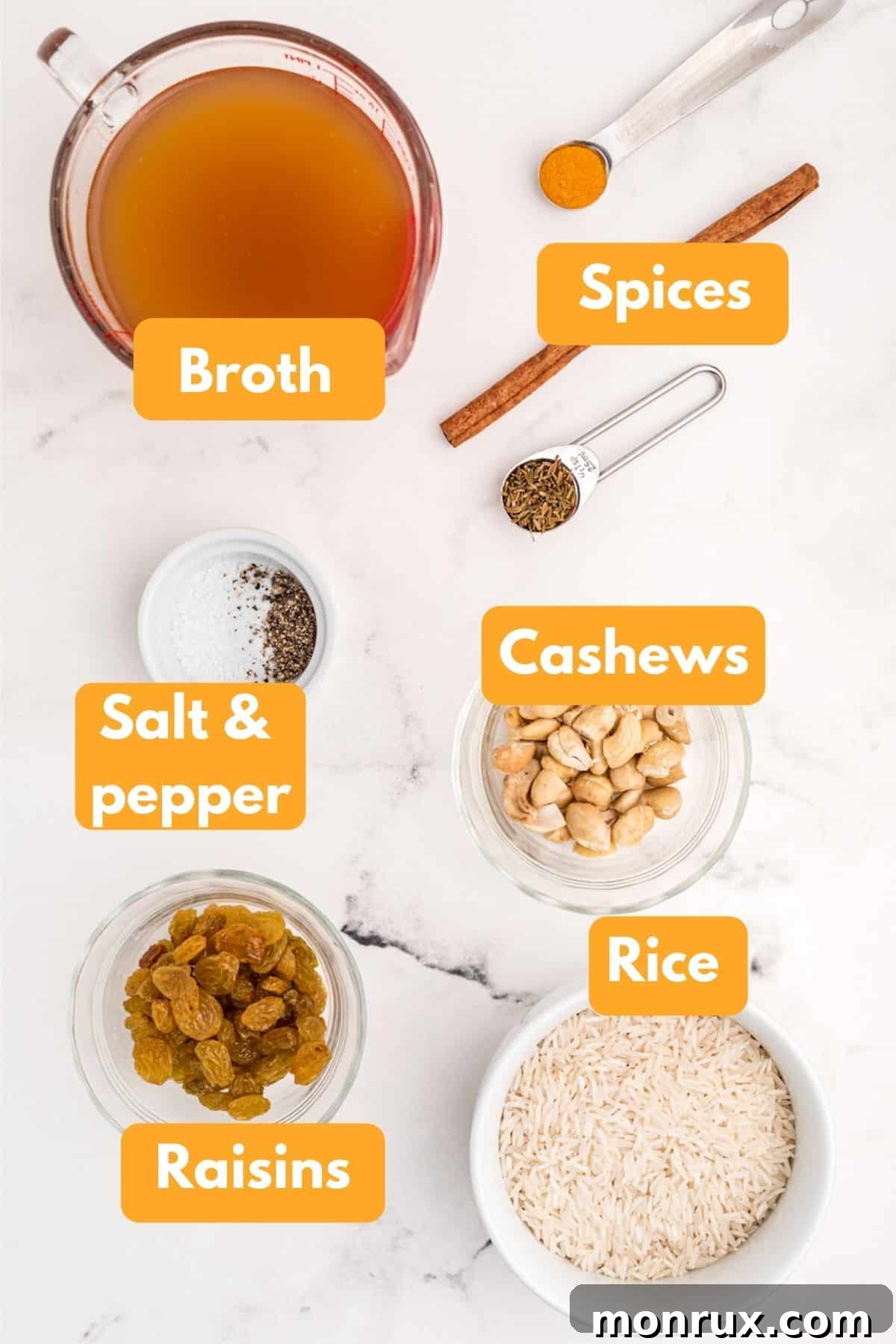 Labeled ingredient photo showing long-grain basmati rice, vegetable broth, ground turmeric, cinnamon stick, cumin seeds, golden raisins, and cashews, all neatly arranged for an Indian yellow rice dish.