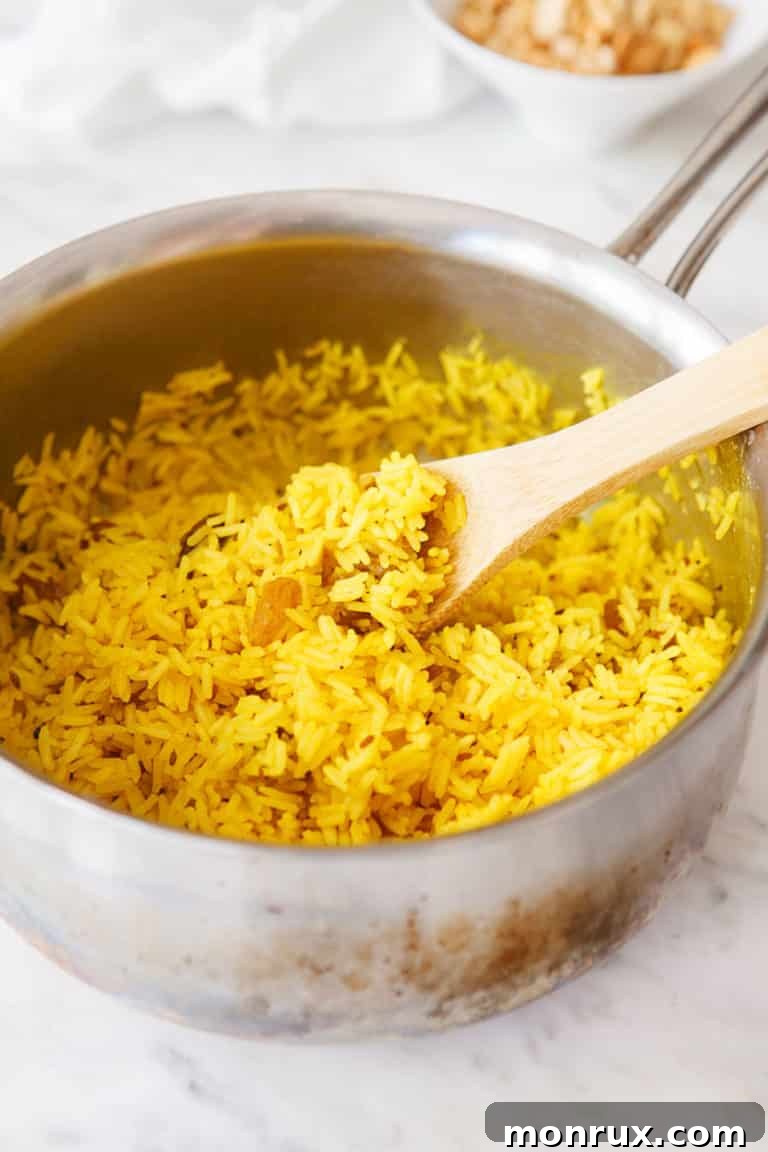 Fluffy yellow rice being gently fluffed with a fork in a saucepan after cooking.