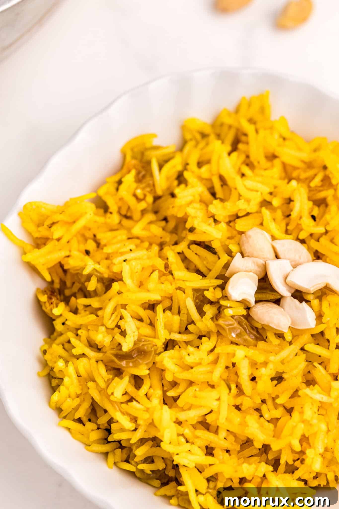 A bowl of Indian yellow rice served with a generous sprinkle of cashews on top, ready to eat.