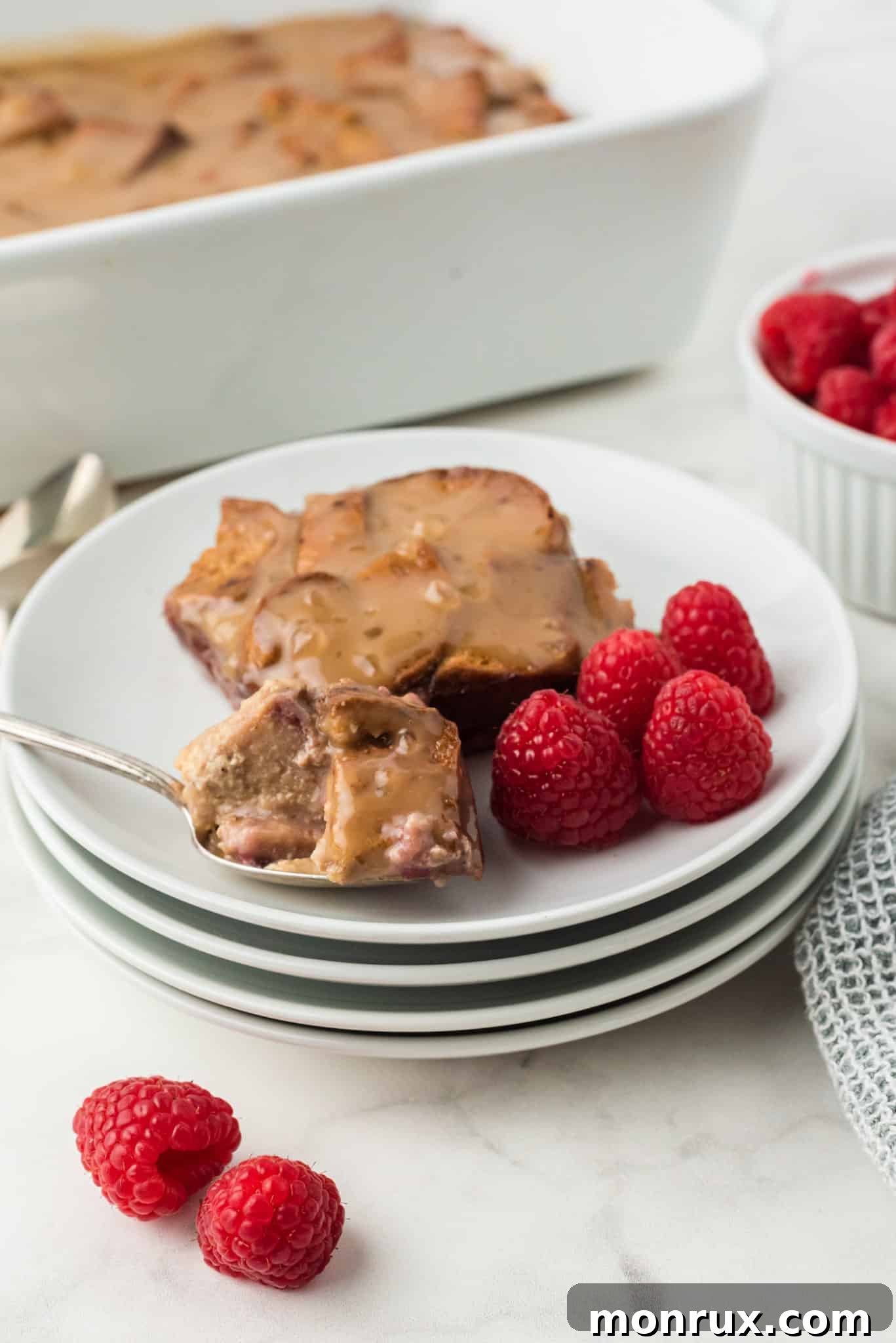 A beautifully presented gluten-free bread pudding on a white plate, adorned with fresh raspberries and a drizzle of vanilla sauce.