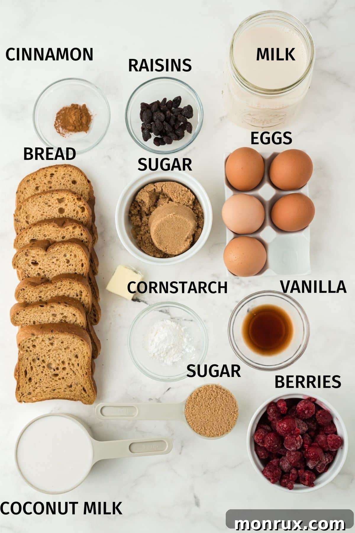 A selection of fresh ingredients laid out for making bread pudding, including gluten-free bread, eggs, raspberries, and coconut milk, all clearly labeled.