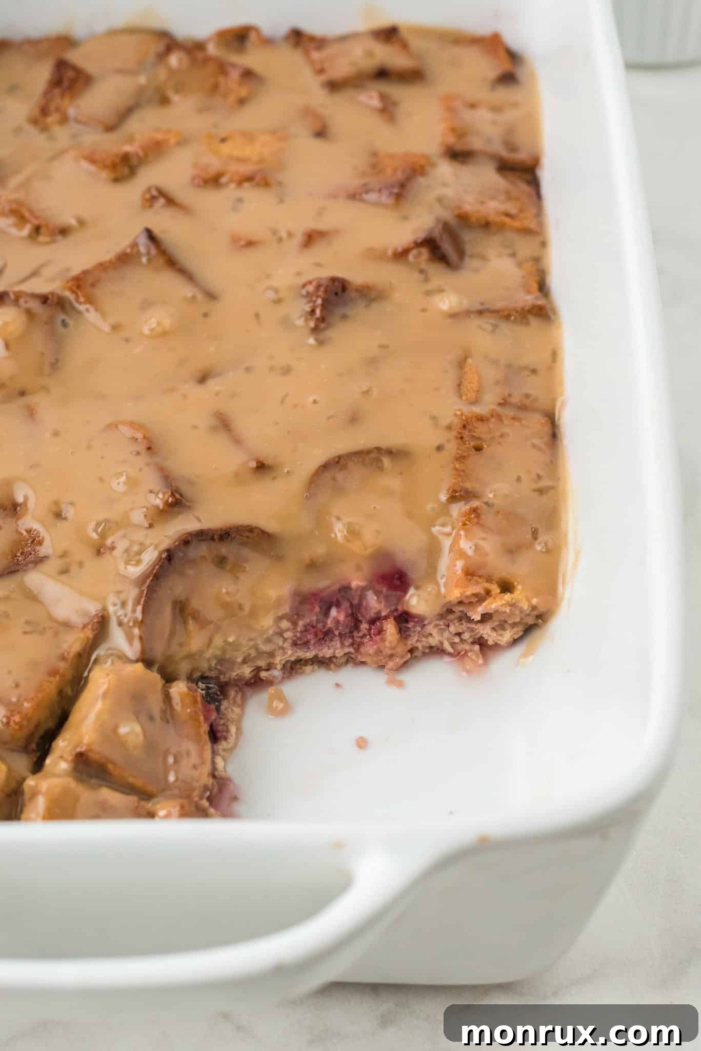 Close-up of a serving of gluten-free bread pudding drizzled with creamy vanilla sauce, garnished with fresh raspberries.