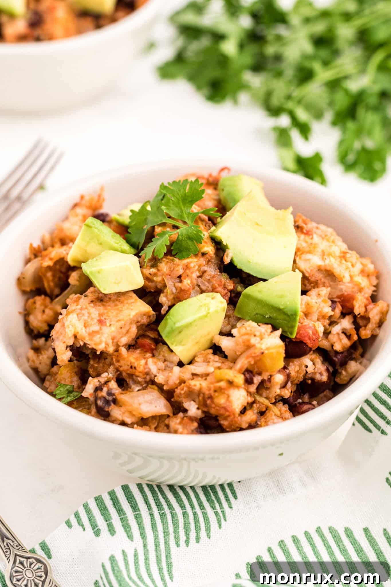 A vibrant bowl of Crockpot Mexican Chicken and Rice, garnished with fresh cilantro and creamy avocado slices.