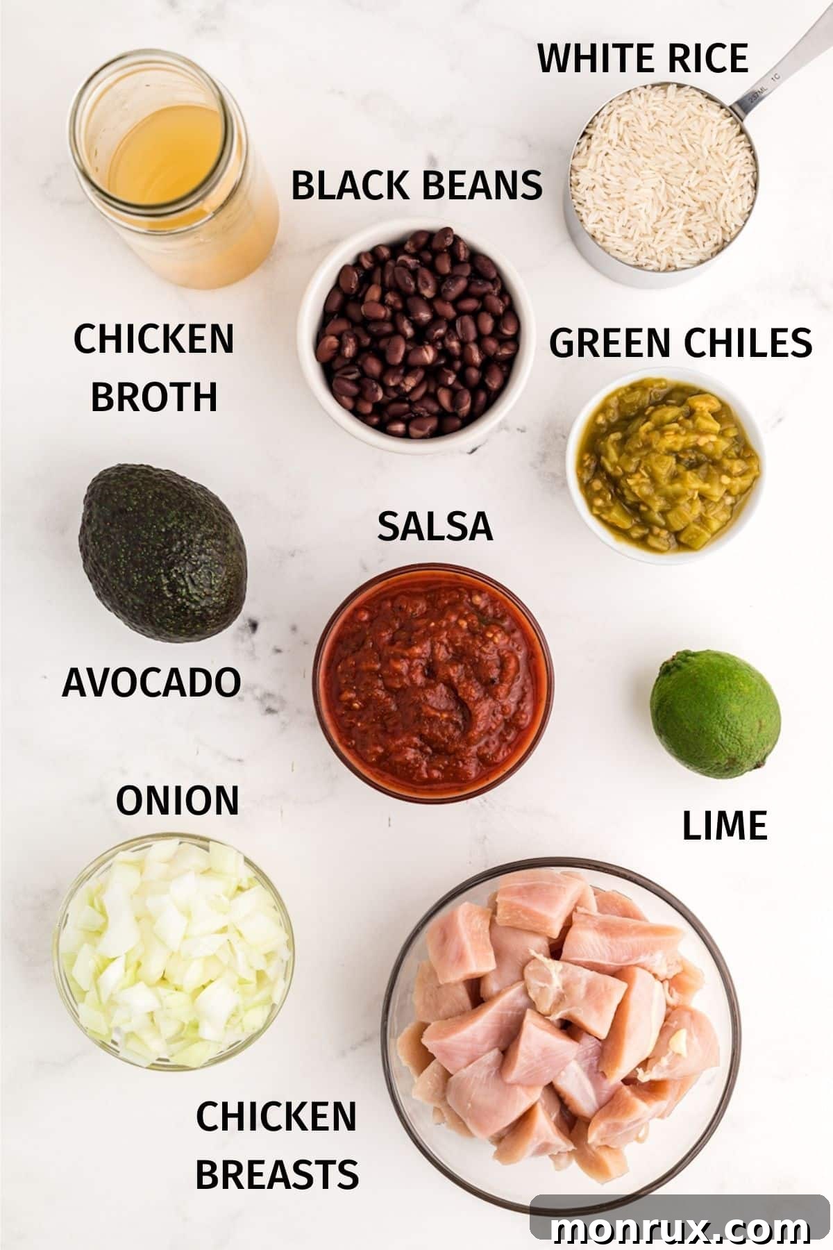 A flat lay photograph showcasing the fresh ingredients for Mexican chicken and rice, including chicken breast, rice, black beans, salsa, onion, and lime.