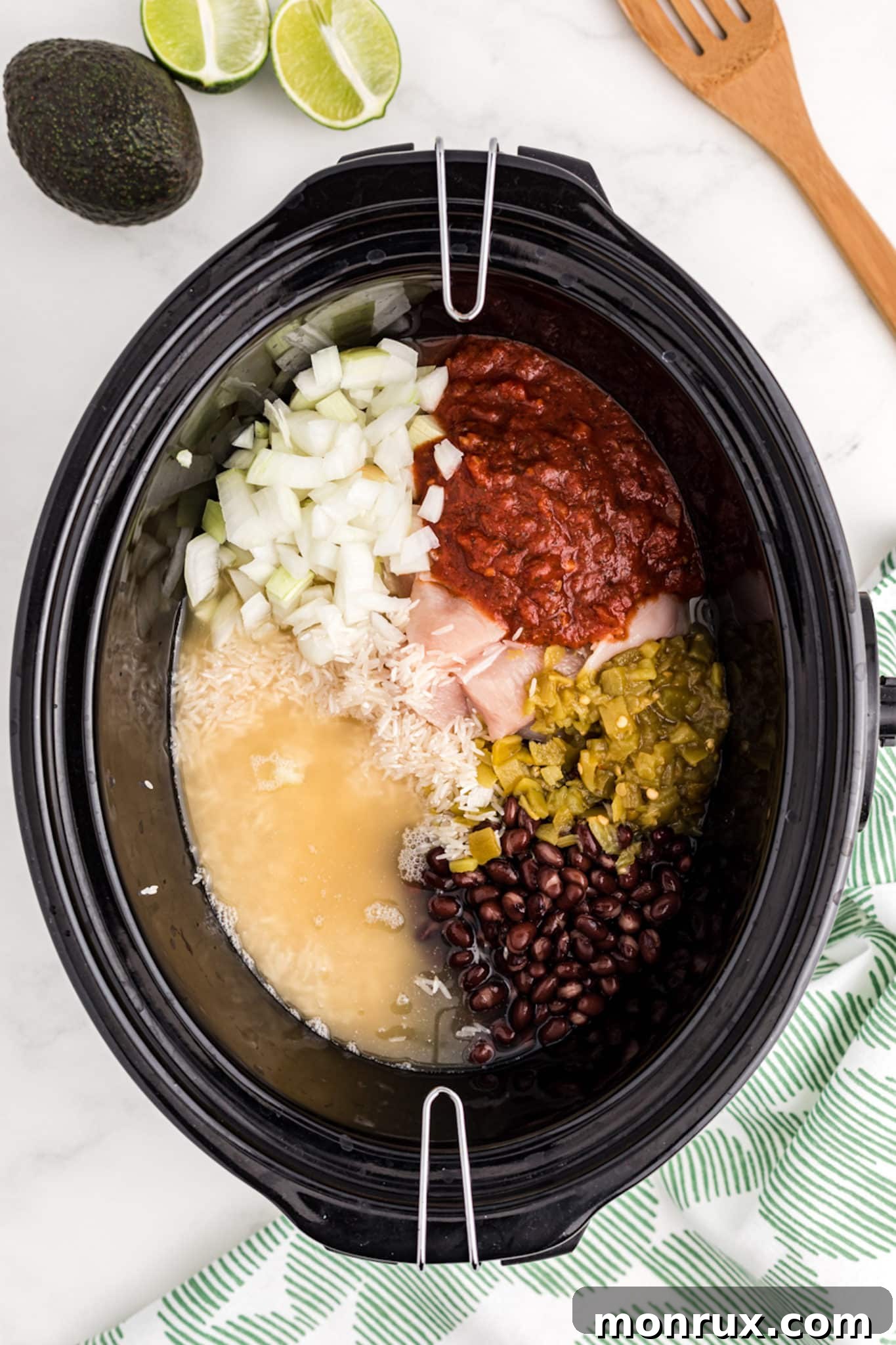 A crockpot filled with uncooked chicken, rice, salsa, and black beans, ready for slow cooking.