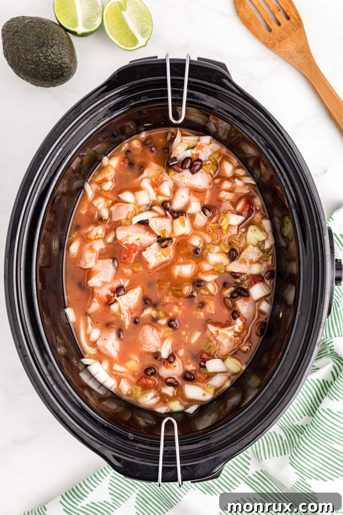 A crockpot containing a broth, chicken, and rice mixture, halfway through the cooking process.