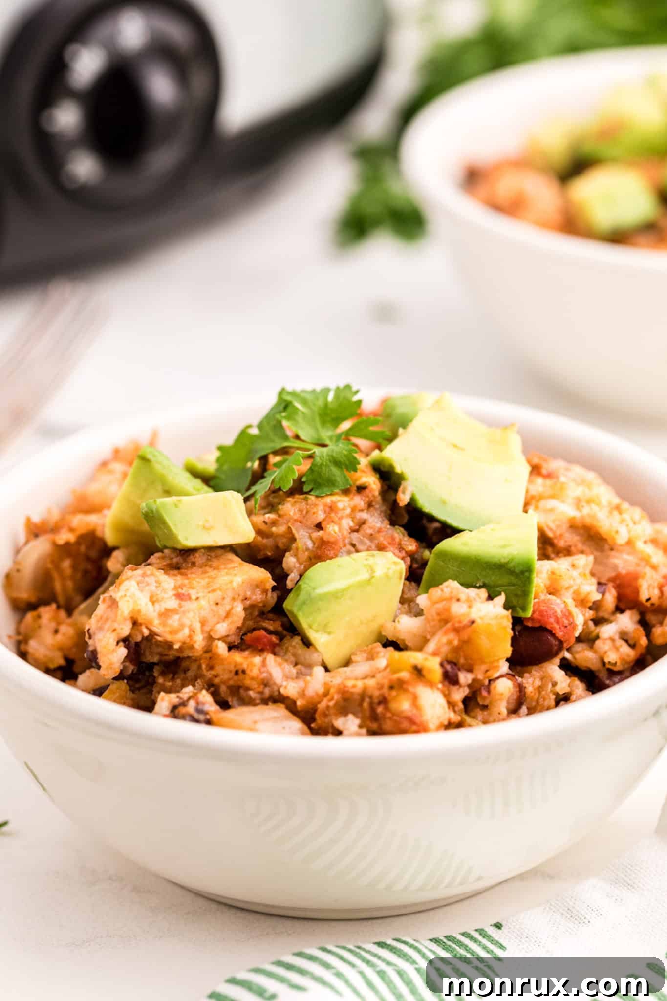A colorful bowl of chicken and rice with avocado, fresh herbs, and lime wedges.