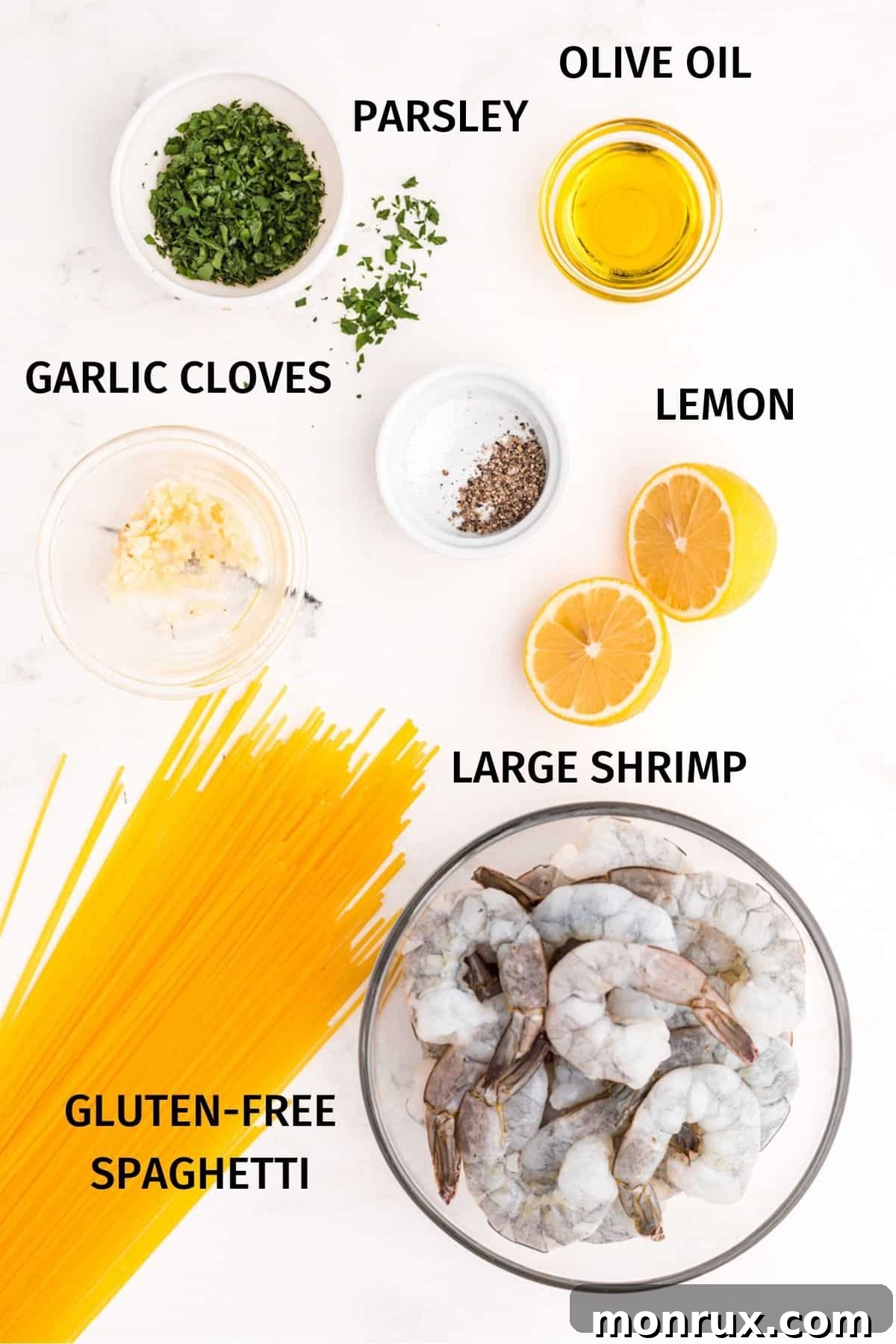 A meticulously arranged flat lay of key shrimp scampi ingredients including glistening olive oil, fresh green parsley, coarse sea salt, bright yellow lemon, pungent garlic cloves, raw pink shrimp, and a bundle of uncooked gluten-free spaghetti.
