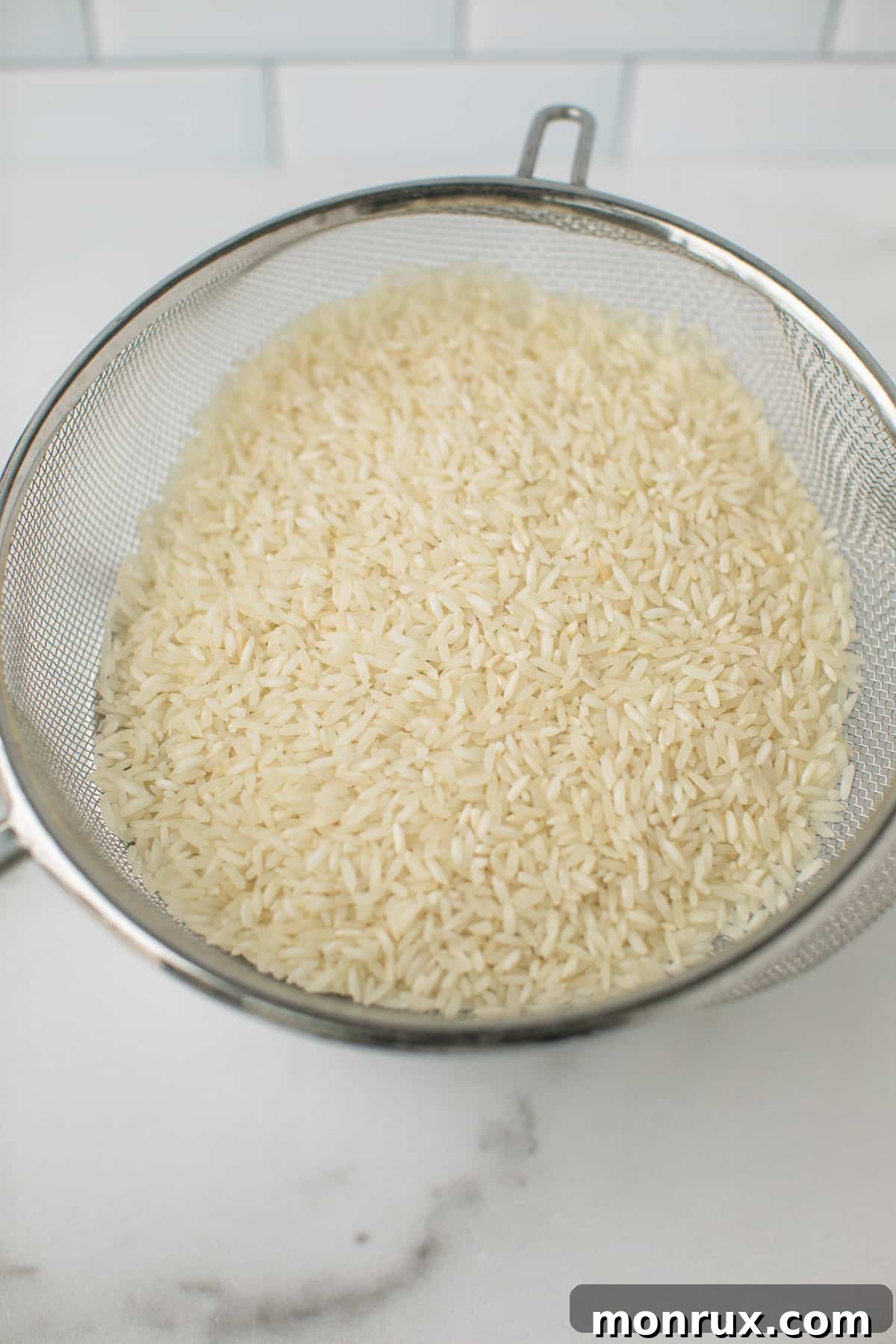 Close-up of white rice being rinsed in a fine mesh colander, showing the water running clear, an essential step for perfect Instant Pot coconut rice.