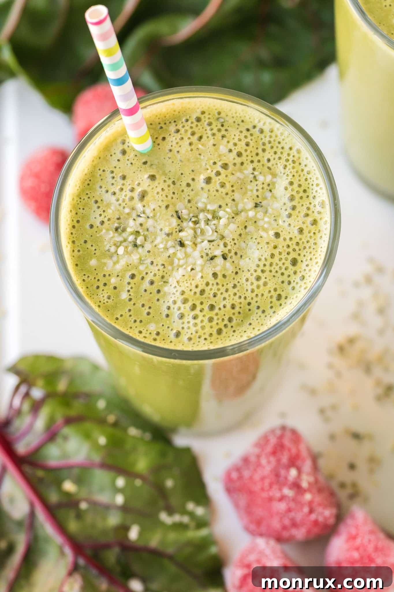 Overhead shot of a vibrant green smoothie with a striped straw and a sprinkle of hemp seeds on top, emphasizing its freshness.