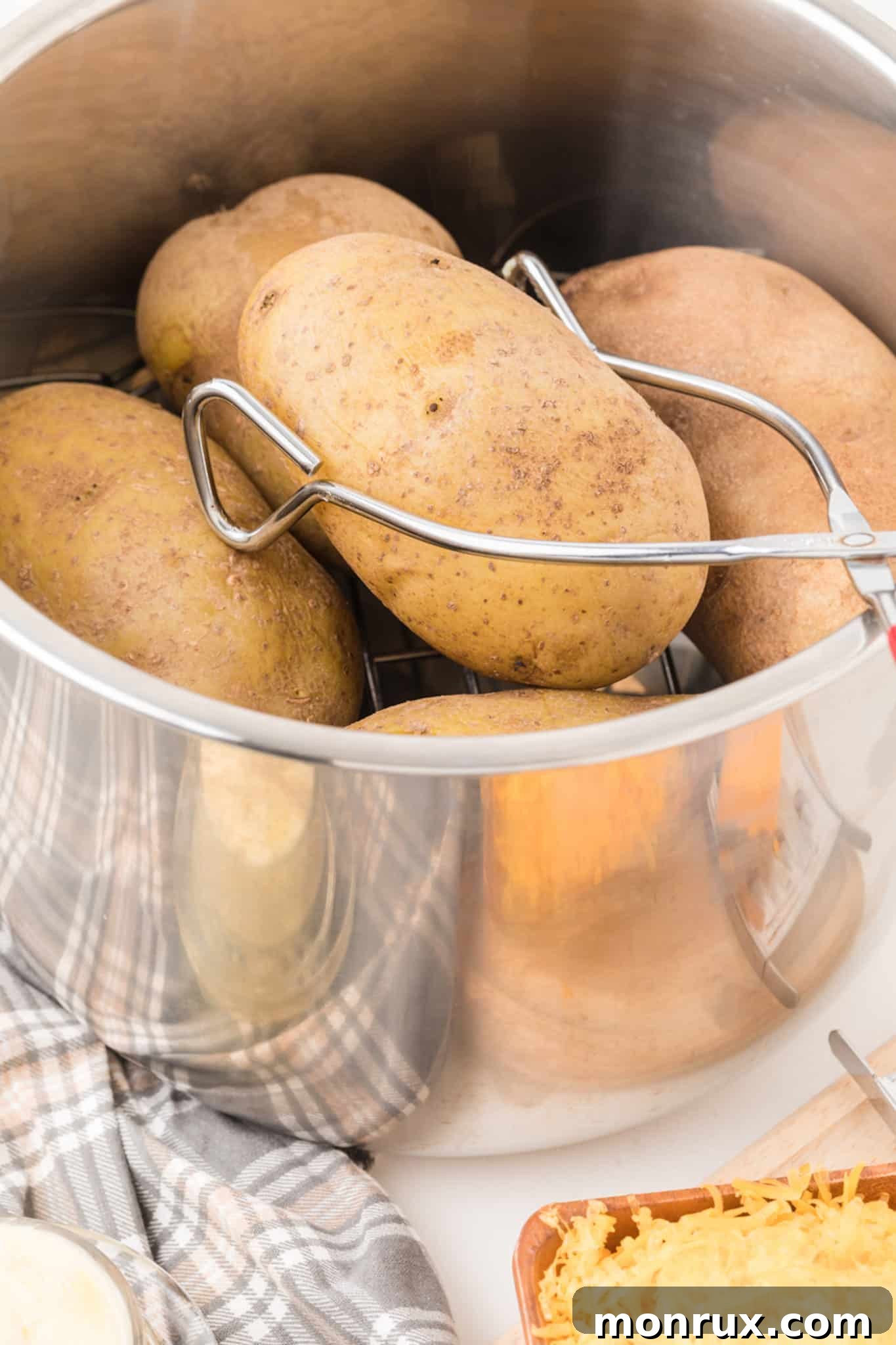 Tongs carefully lifting a perfectly cooked Instant Pot baked potato from the inner pot.