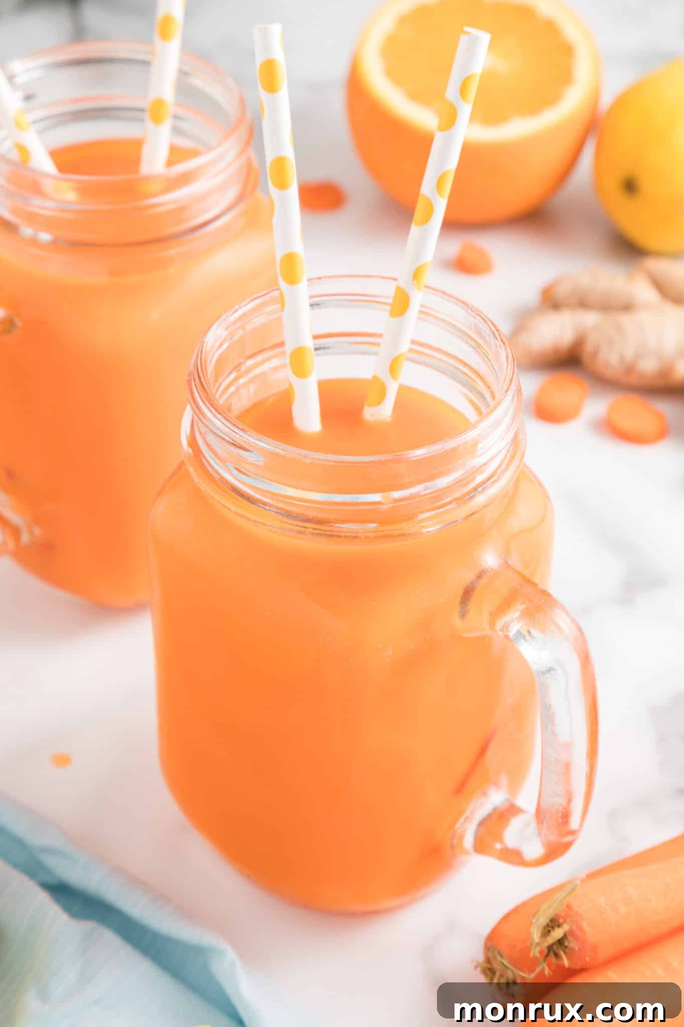 Two mason jar mugs with vibrant carrot juice, each with two straws, set against a bright background.