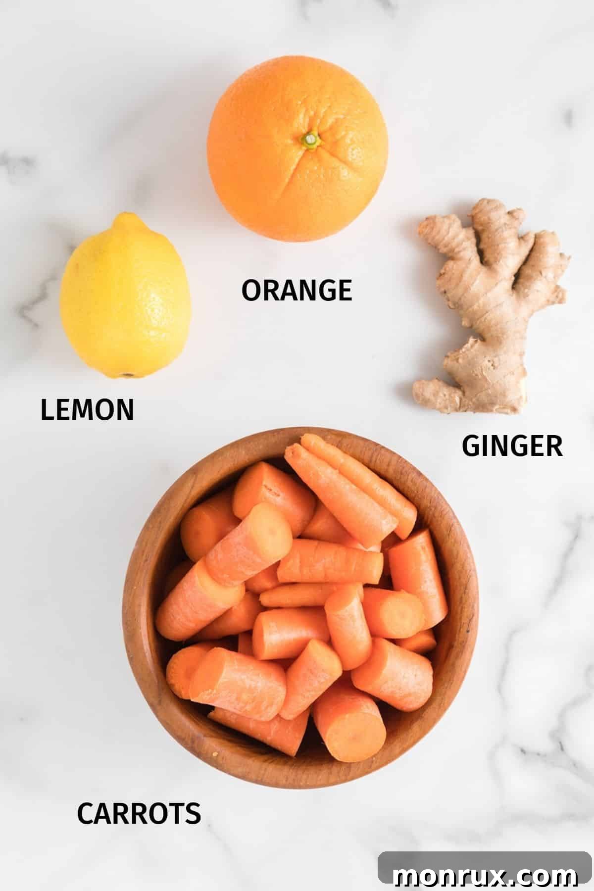 Fresh carrots, oranges, lemon, and ginger root laid out on a clean white surface, ready for juicing.