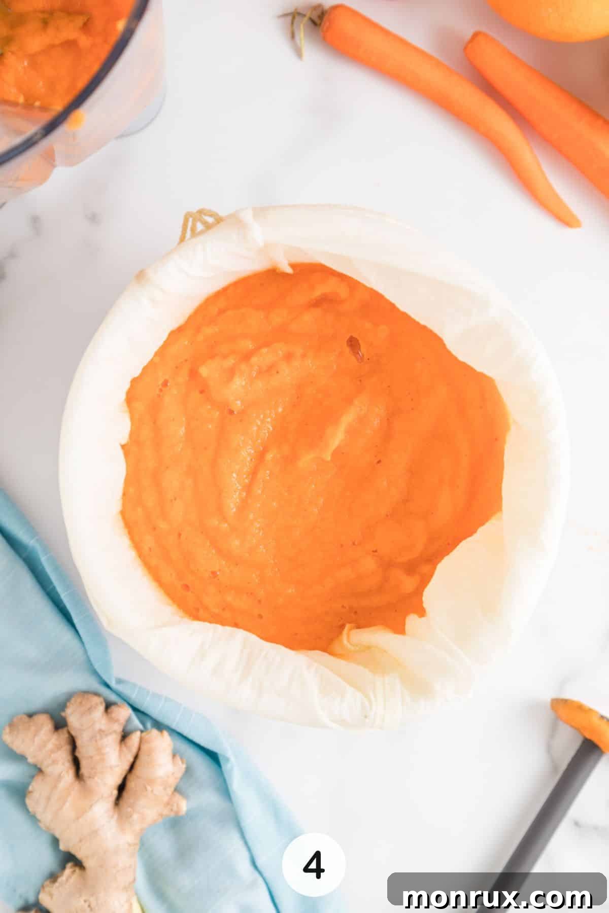Fourth step of making carrot juice: blended carrot mixture in a nut milk bag over a bowl, ready for straining.
