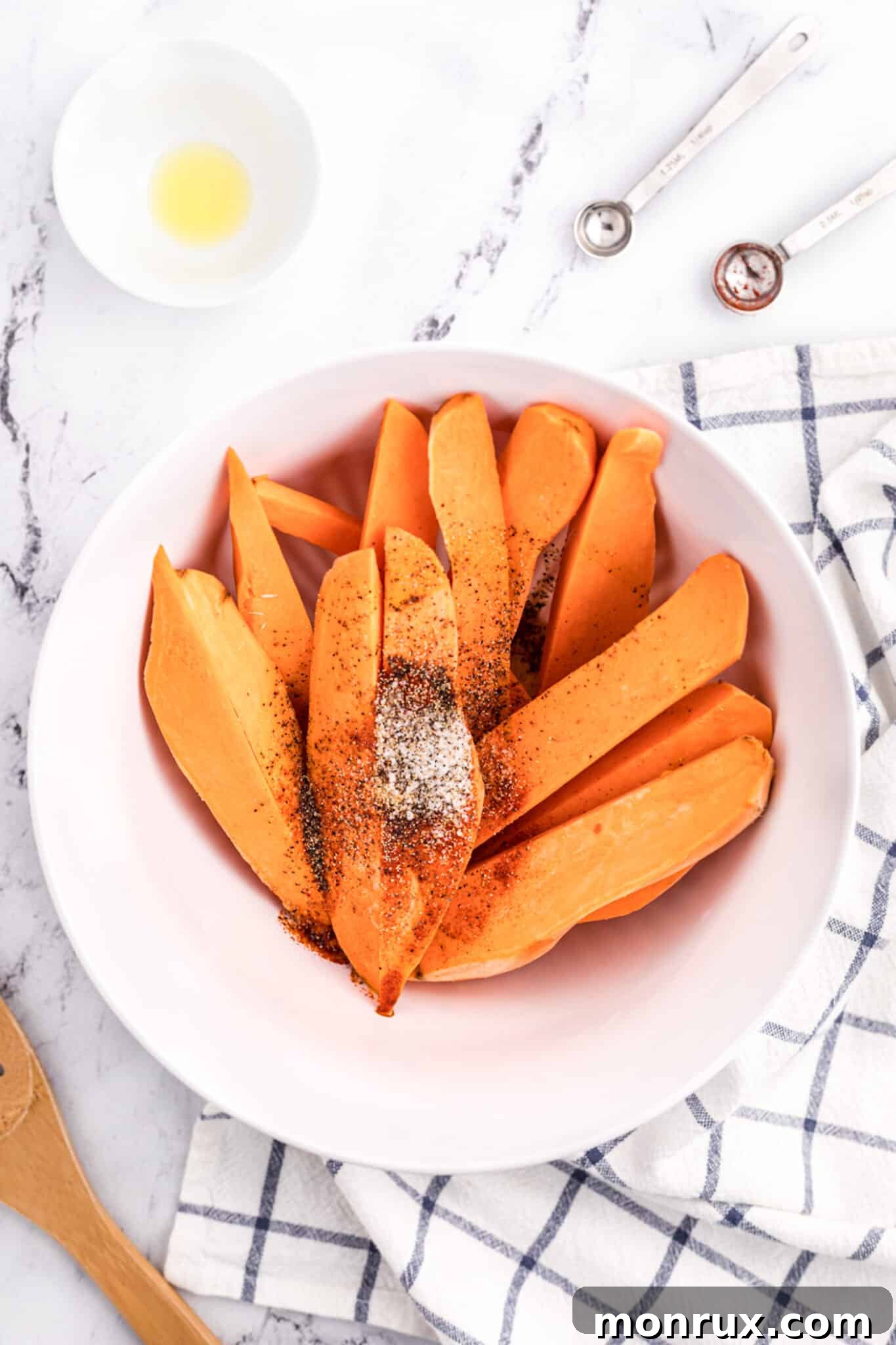 Sweet potato wedges in a bowl, coated with oil and seasonings.